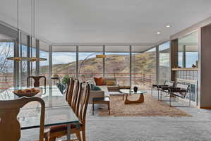 Open-concept living space featuring floor-to-ceiling windows, a glass-top dining table, recessed lighting, a fireplace with a tile surround, and a balcony with a railing overlooking mountains