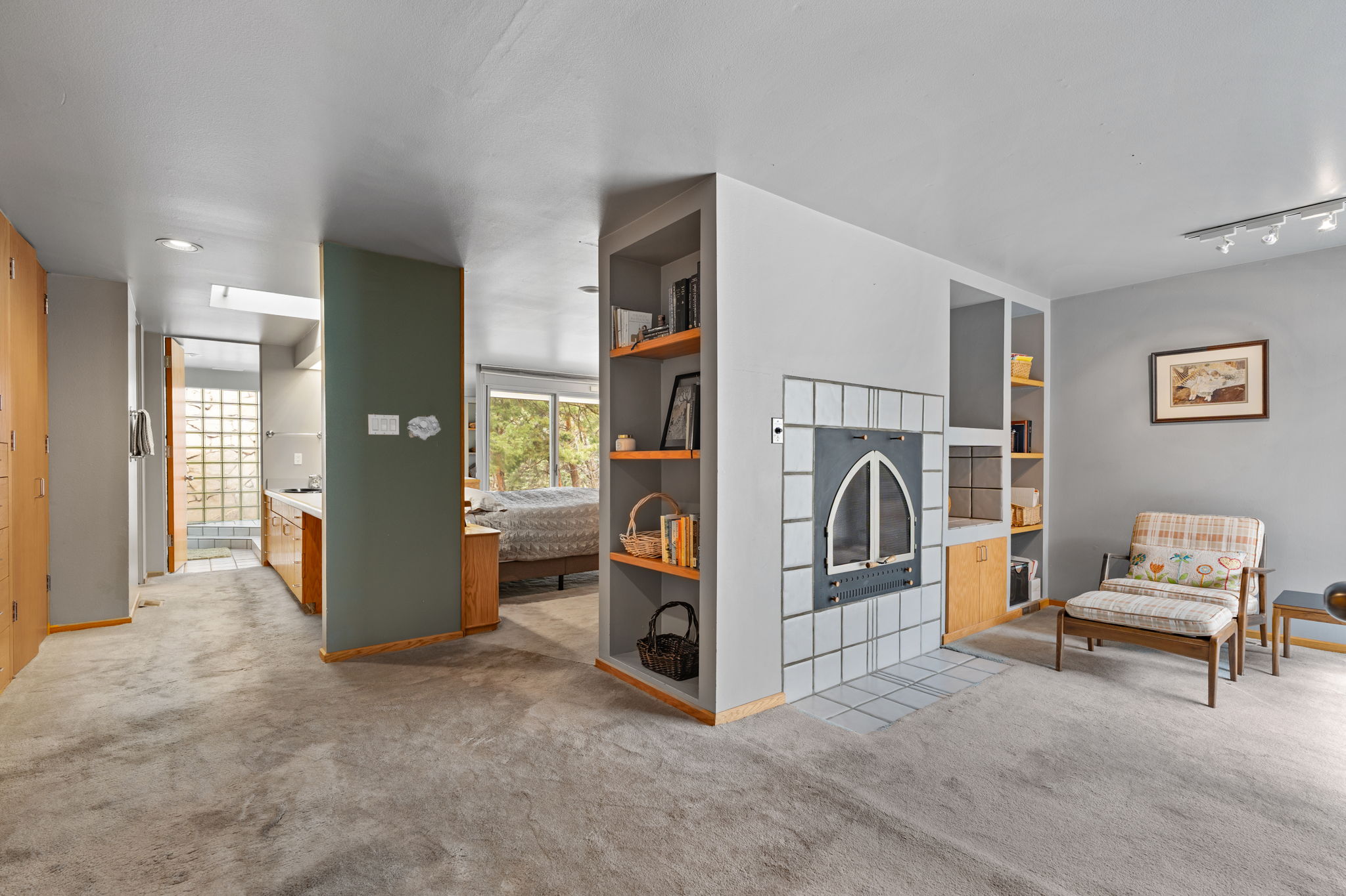 Living area featuring a tiled fireplace with an arched insert, built-in shelving, wood-finish cabinetry, and track lighting