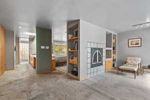 Living area featuring a tiled fireplace with an arched insert, built-in shelving, wood-finish cabinetry, and track lighting