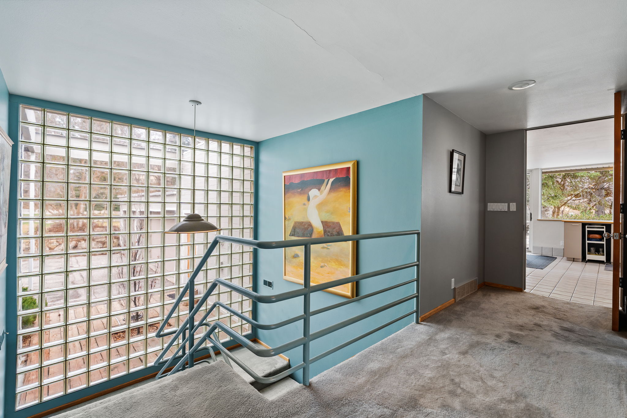 Staircase with glass block wall, metal railing, and carpeted treads