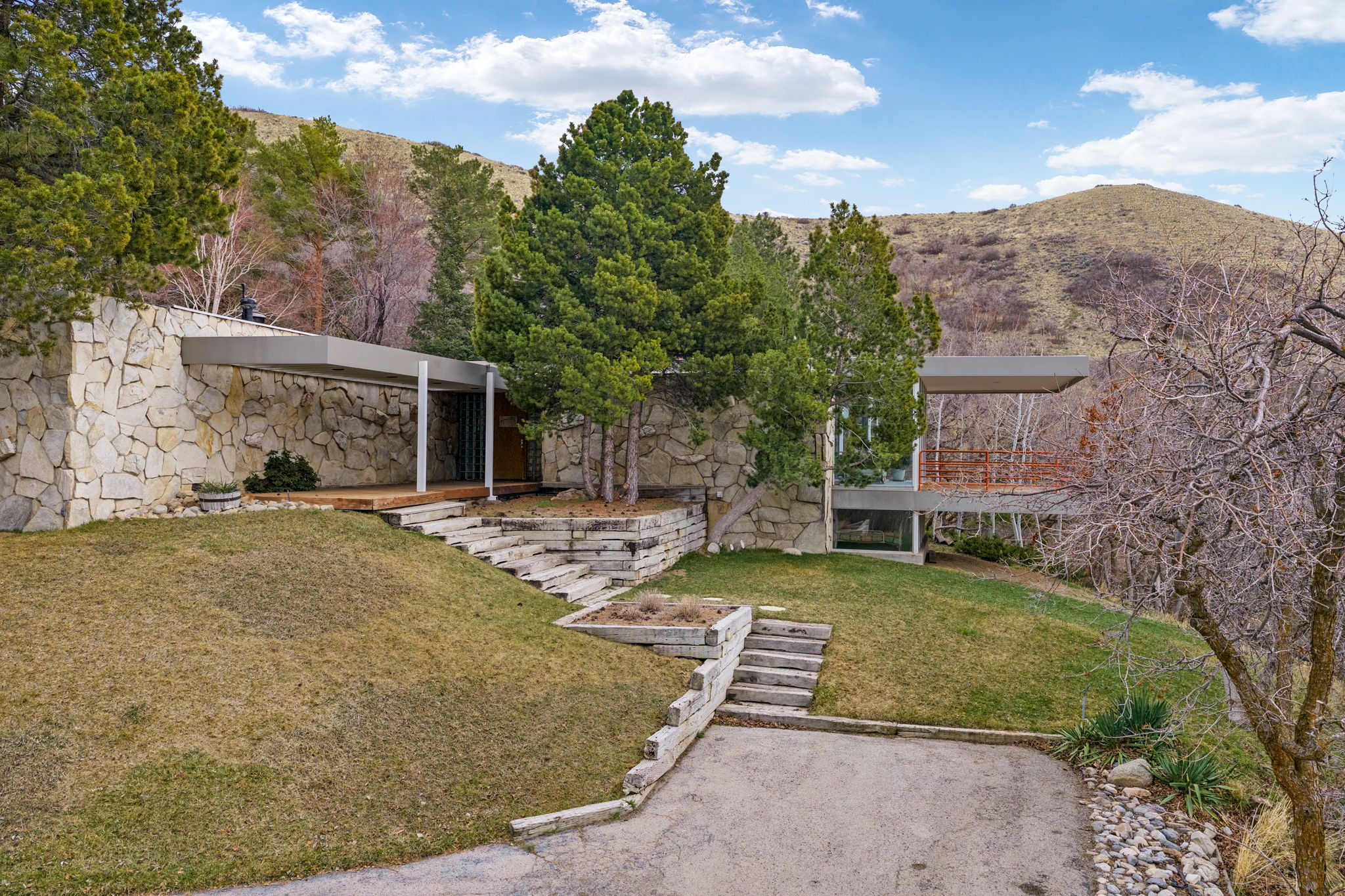 Stone-clad exterior featuring a covered entry, wood decking, and tiered landscaping