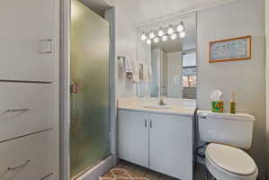Bathroom featuring a vanity with an integrated sink, a rectangular mirror with a multi-bulb light fixture, a toilet, and a shower with a frosted glass door