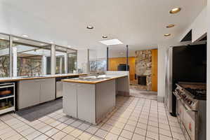 Spacious kitchen featuring floor-to-ceiling windows, a central island with integrated sink, and white square tile flooring