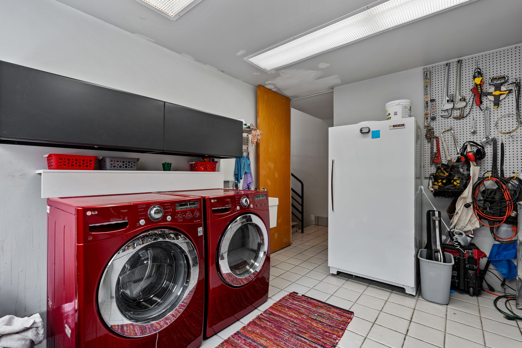 Dedicated utility space featuring a tiled floor, overhead fluorescent lighting, and a wall-mounted pegboard for organization