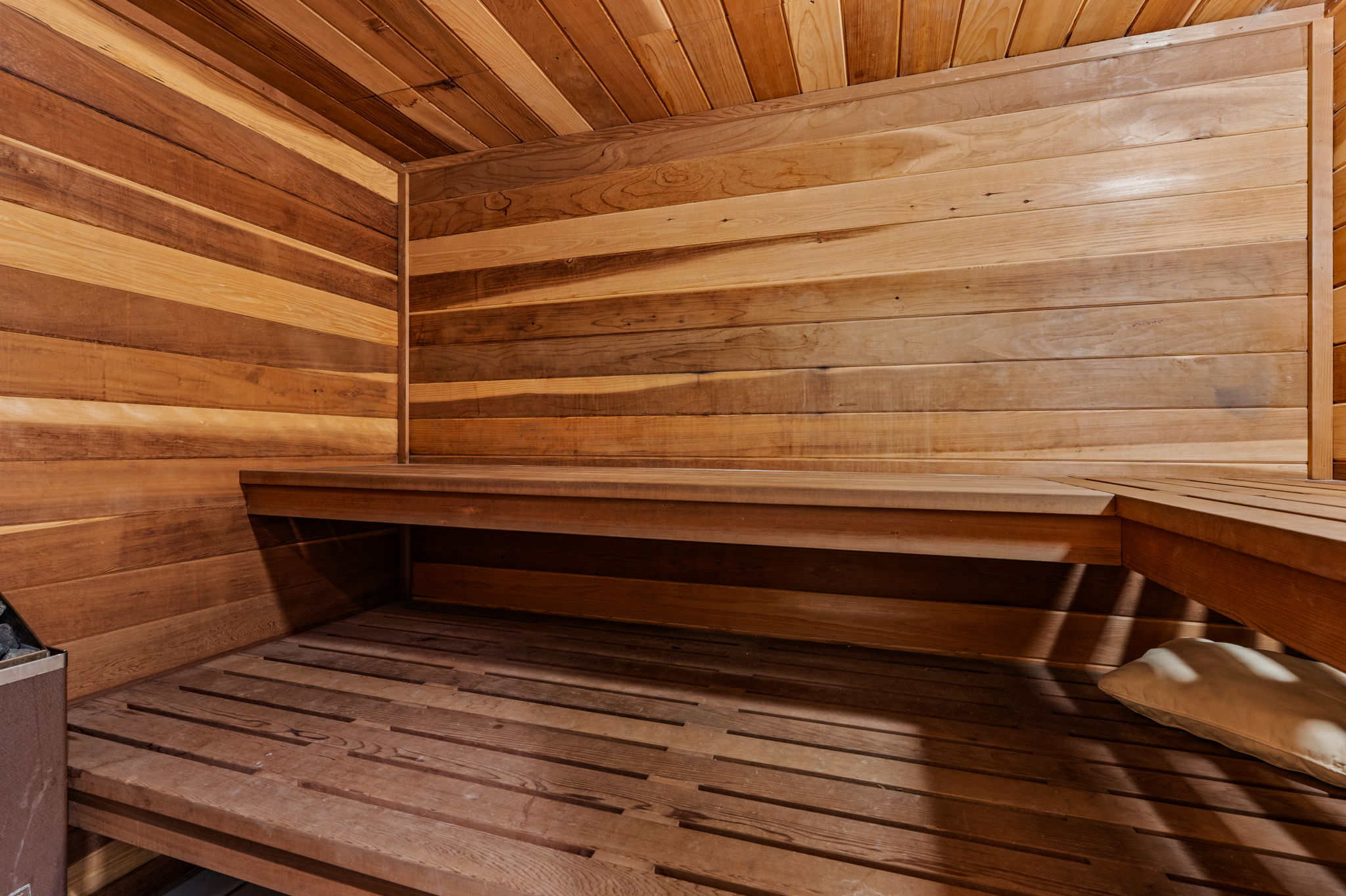Custom sauna featuring warm wood paneling, slatted wood flooring, and built-in benches
