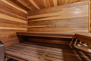 Custom sauna featuring warm wood paneling, slatted wood flooring, and built-in benches