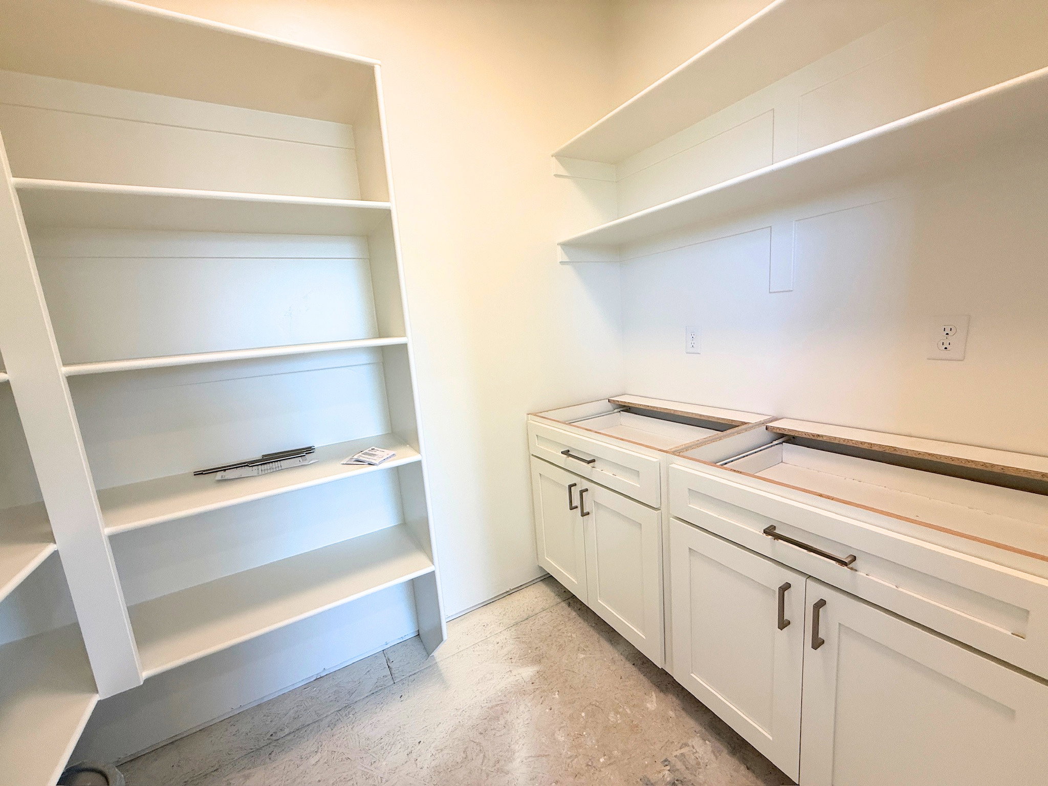 Utility room featuring white shaker-style base cabinets, ample built-in shelving, white wall shelving, and bronze hardware