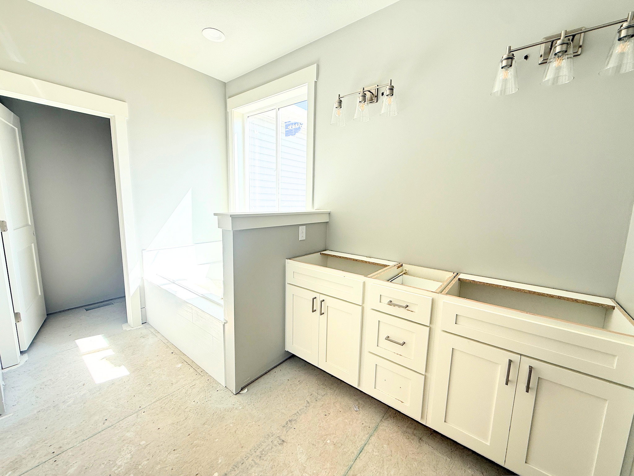 Bathroom featuring light grey wall paint, a built-in bathtub with a window, recessed ceiling lighting, and two vanity light fixtures with clear glass shades