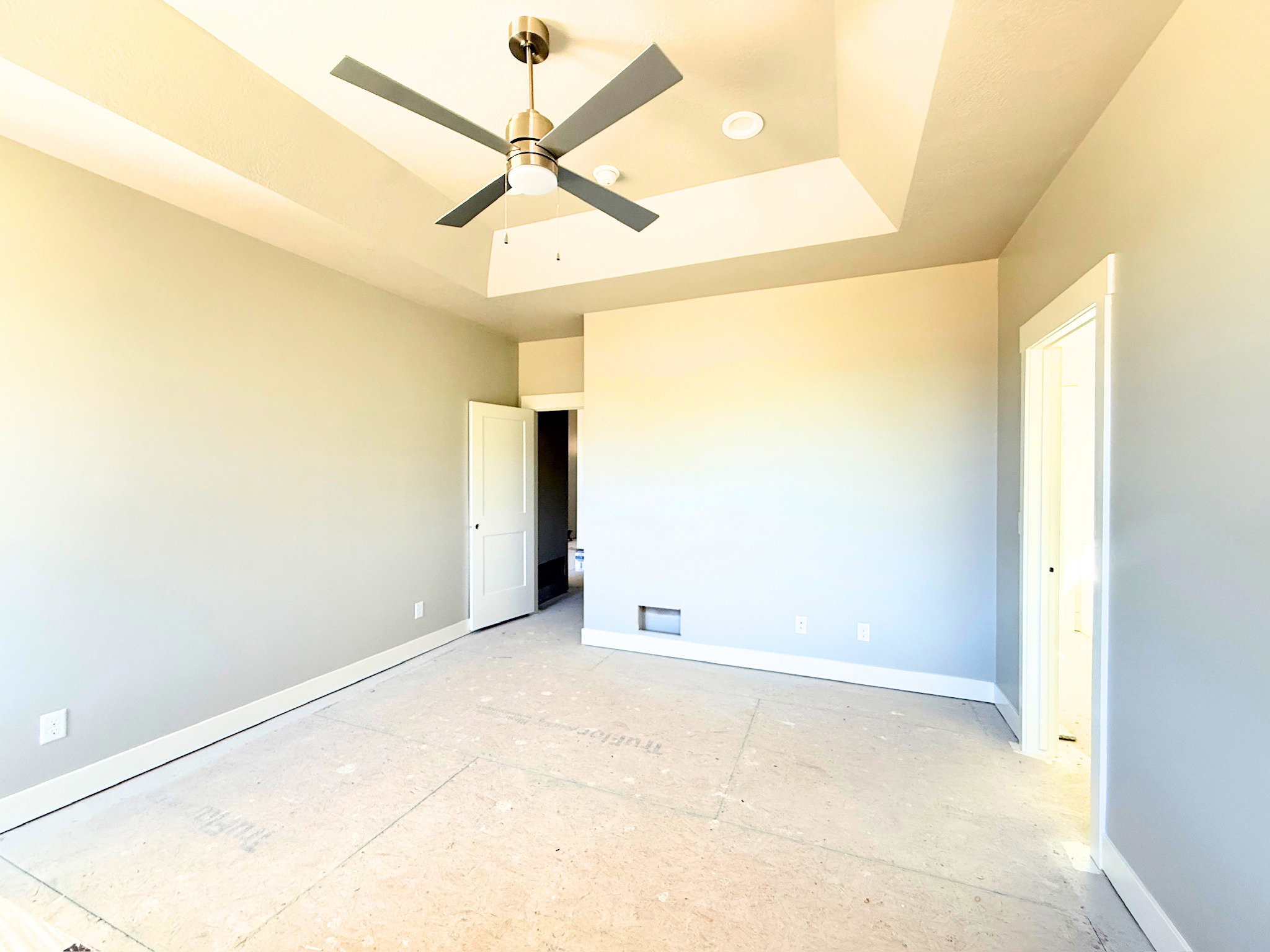 Spacious room featuring a tray ceiling with a modern ceiling fan, recessed lighting, and light gray wall paint