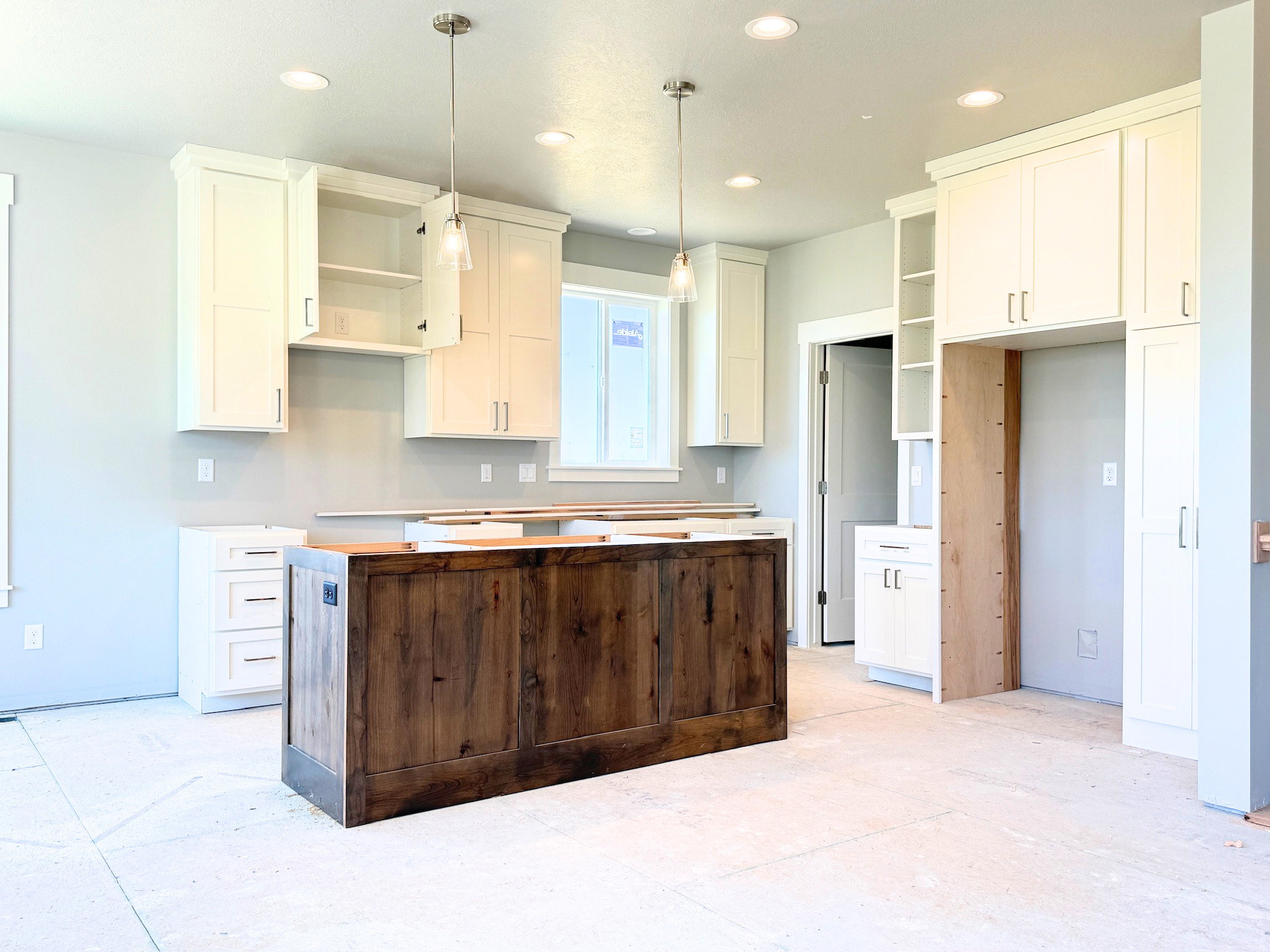 Spacious kitchen featuring a dark wood-finish island, white shaker-style cabinetry, recessed lighting, and pendant lights