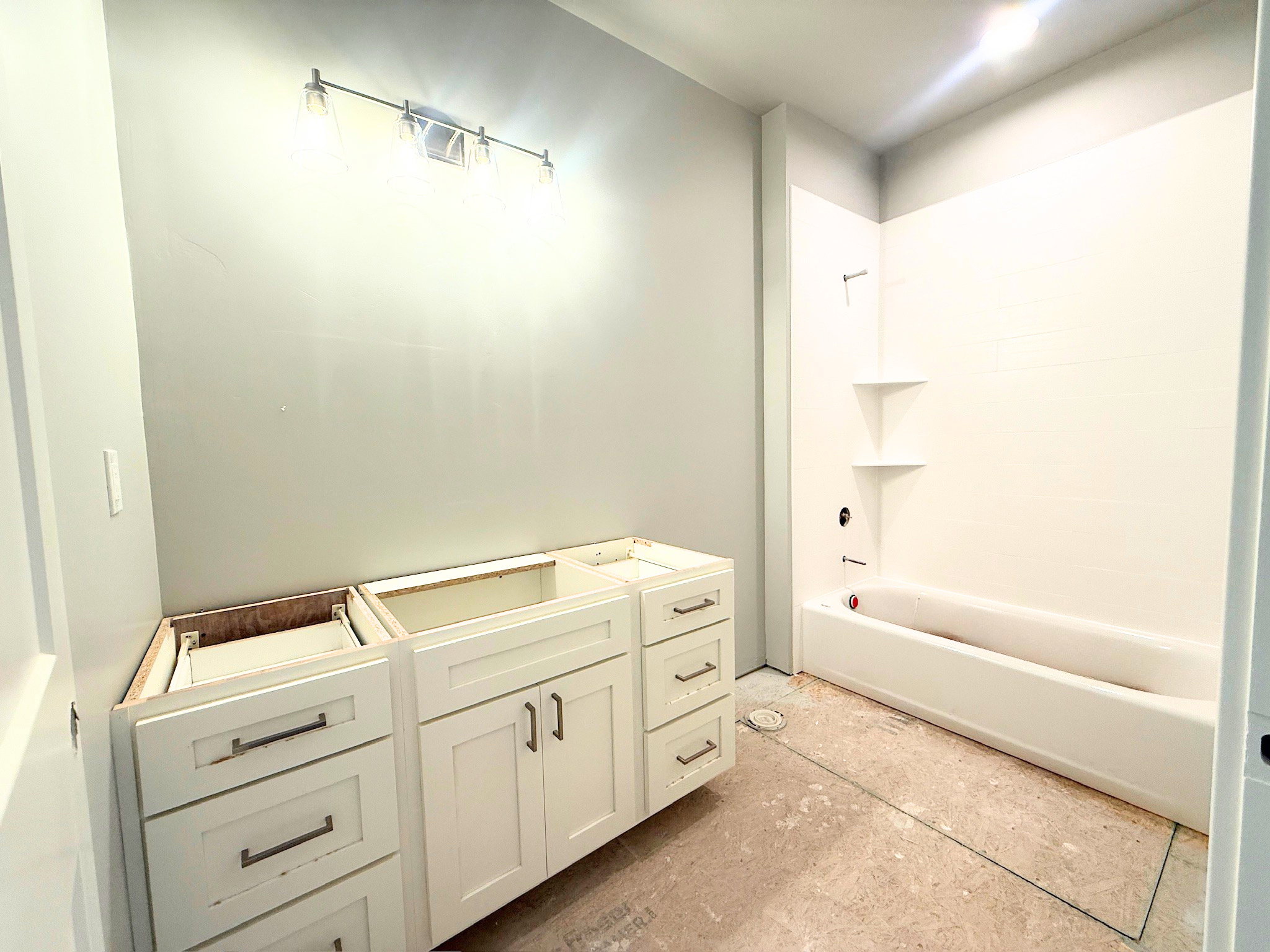 Bathroom featuring a white vanity cabinet with multiple drawers and doors, a modern four-light vanity fixture, and a white tub/shower combination with integrated corner shelving