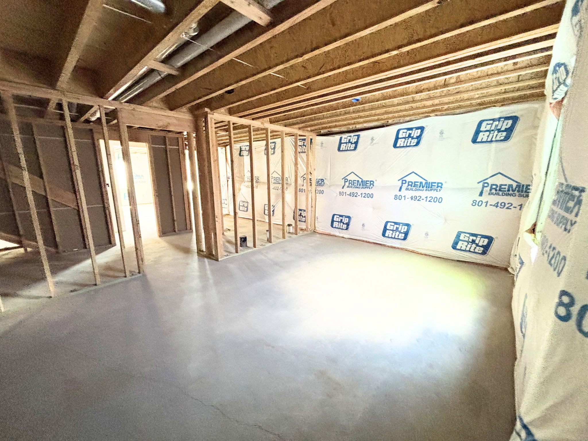 Unfinished interior space featuring a concrete floor, exposed wooden ceiling joists, and framed interior walls