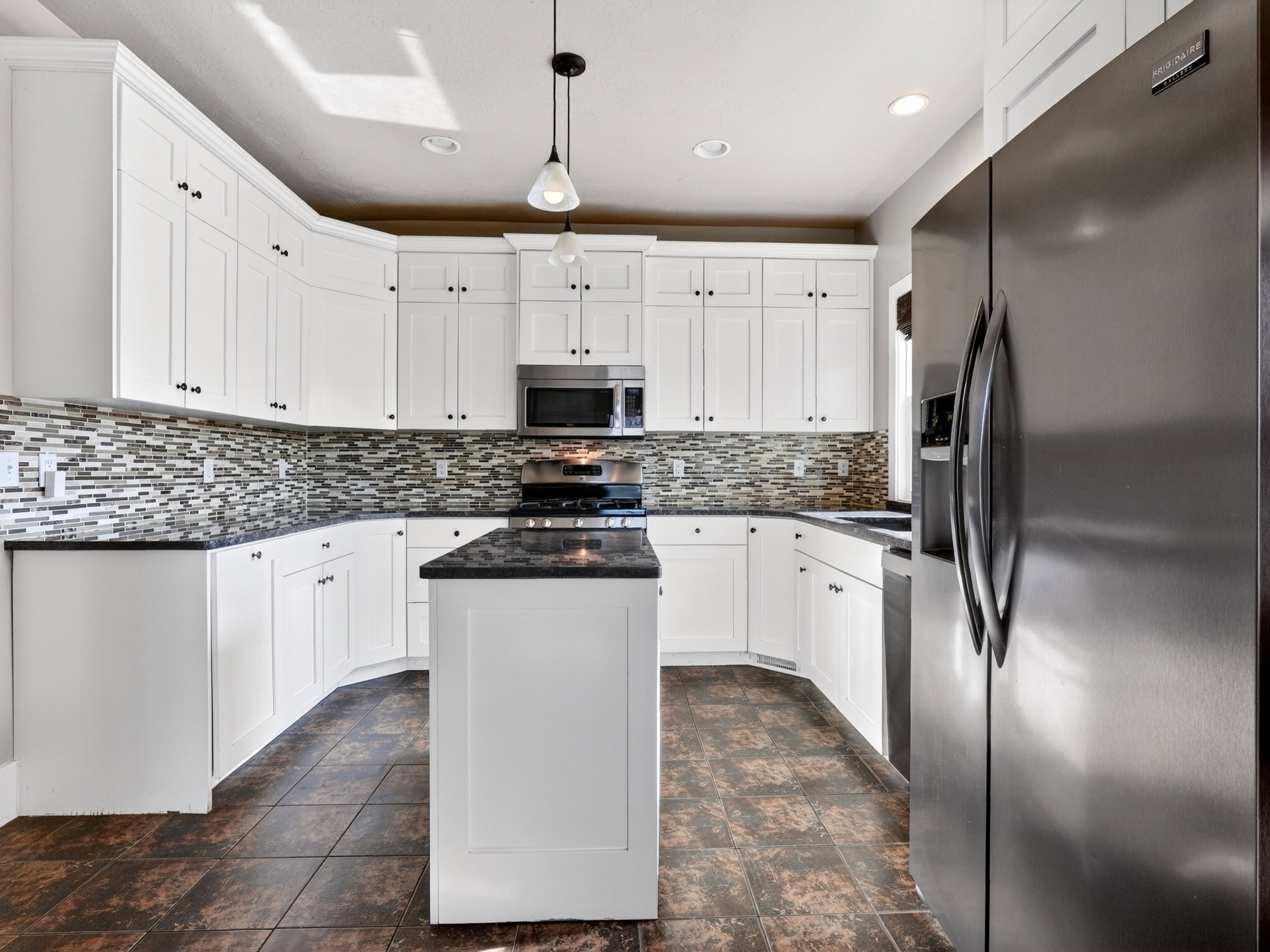 Kitchen featuring white cabinetry, dark countertops, a mosaic tile backsplash, a stainless steel refrigerator, and recessed lighting