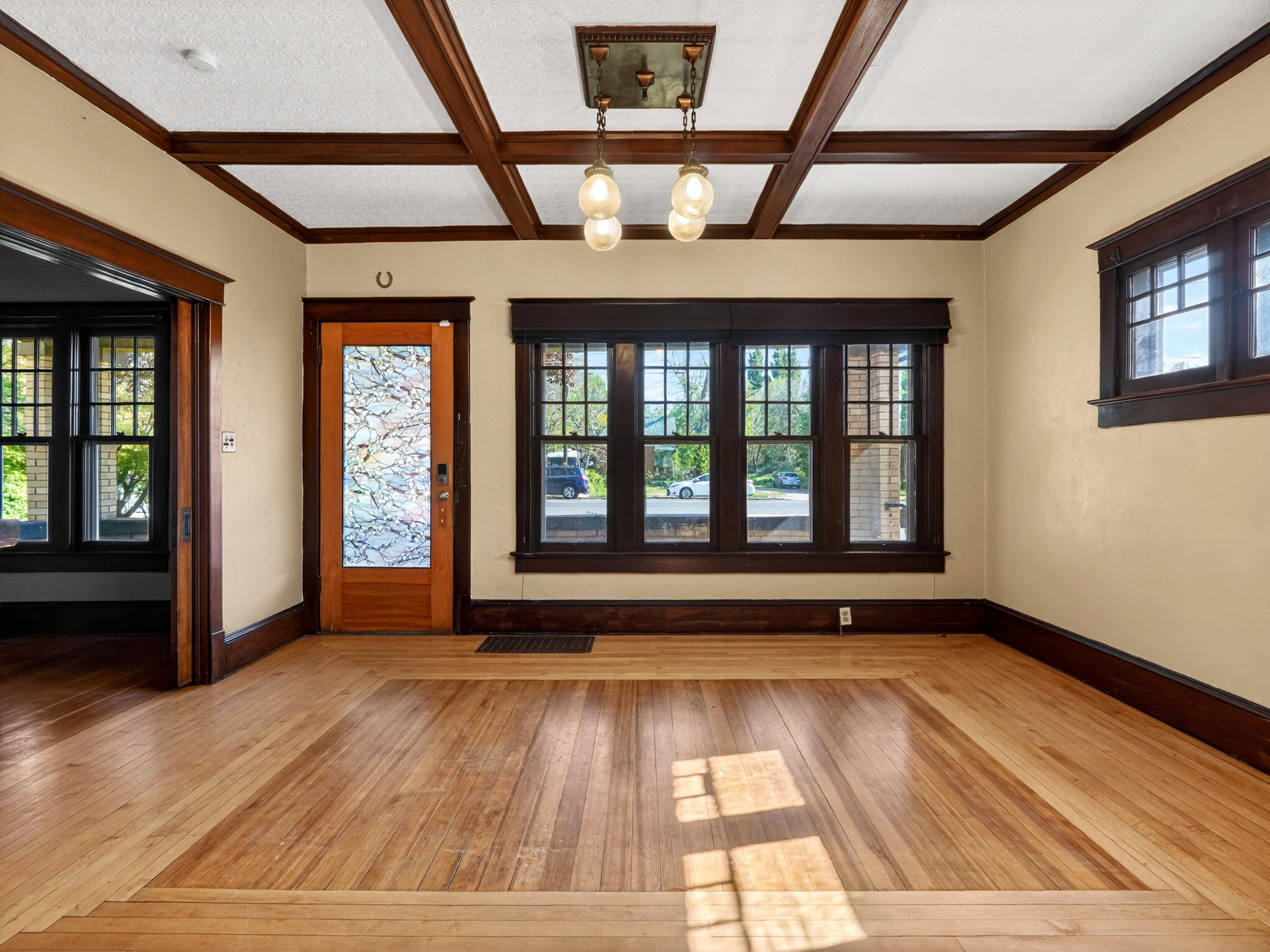Expansive room featuring wood-finish flooring with a border inlay, deep brown trim, and coffered ceilings
