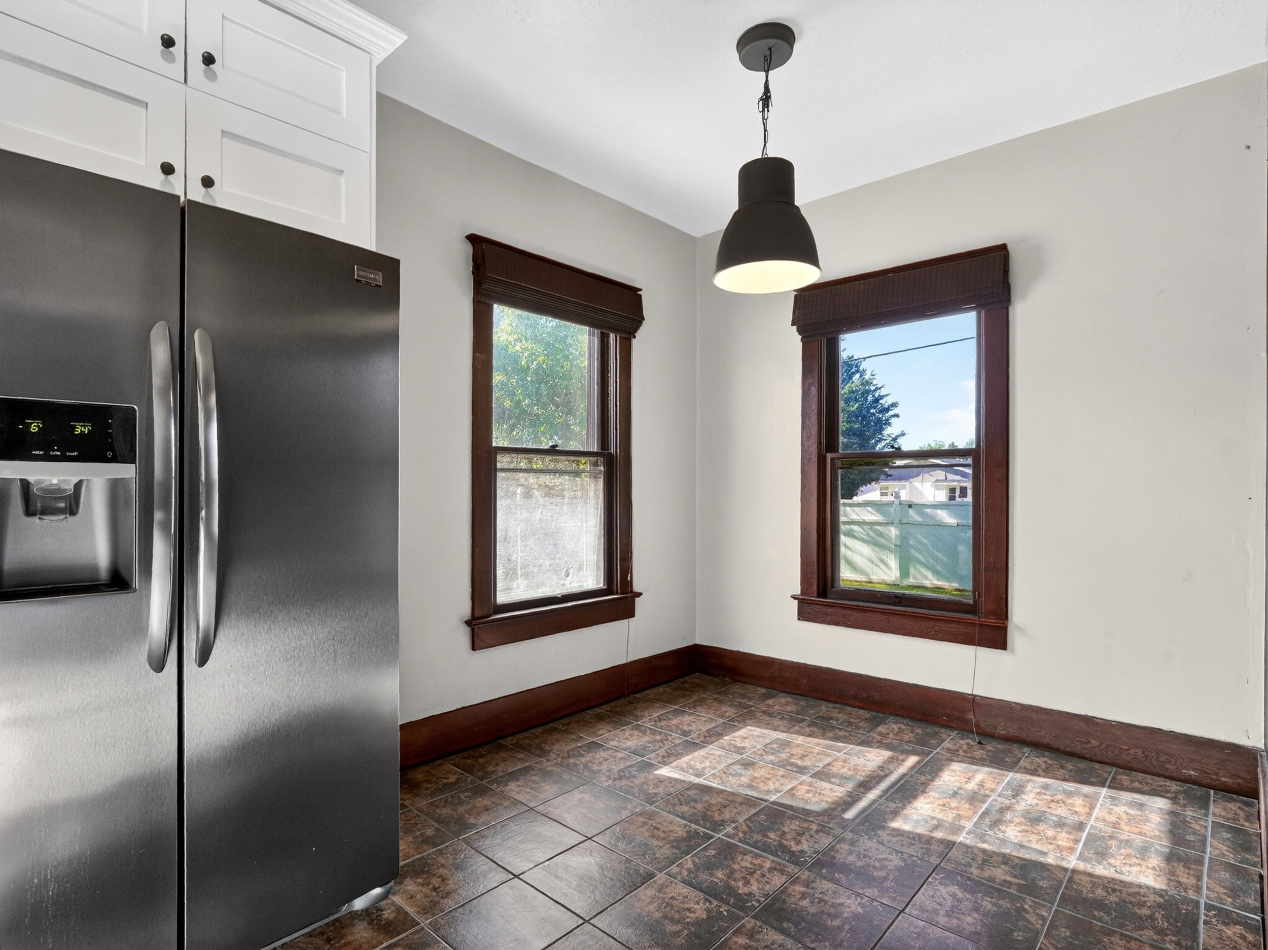 Stainless steel refrigerator with a built-in ice and water dispenser, white upper cabinetry with black hardware, and dark wood-finish window trim