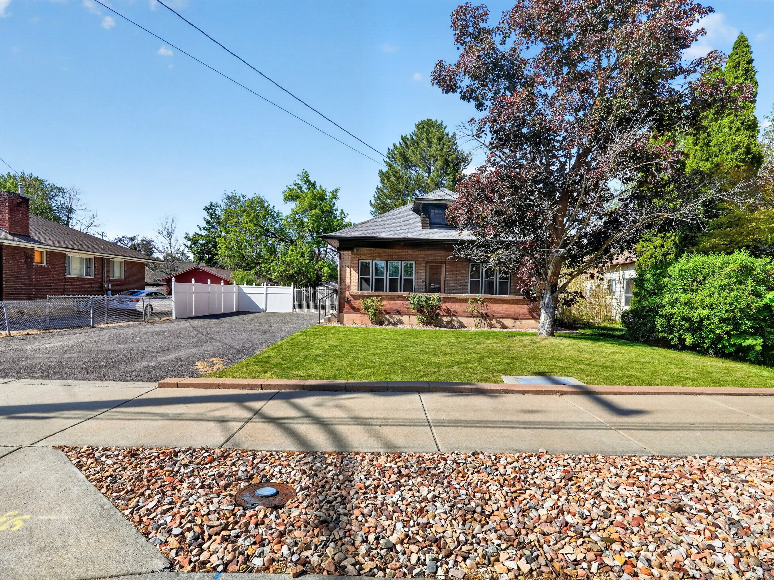 Traditional brick home with a dormer, front lawn, mature tree, and paved driveway