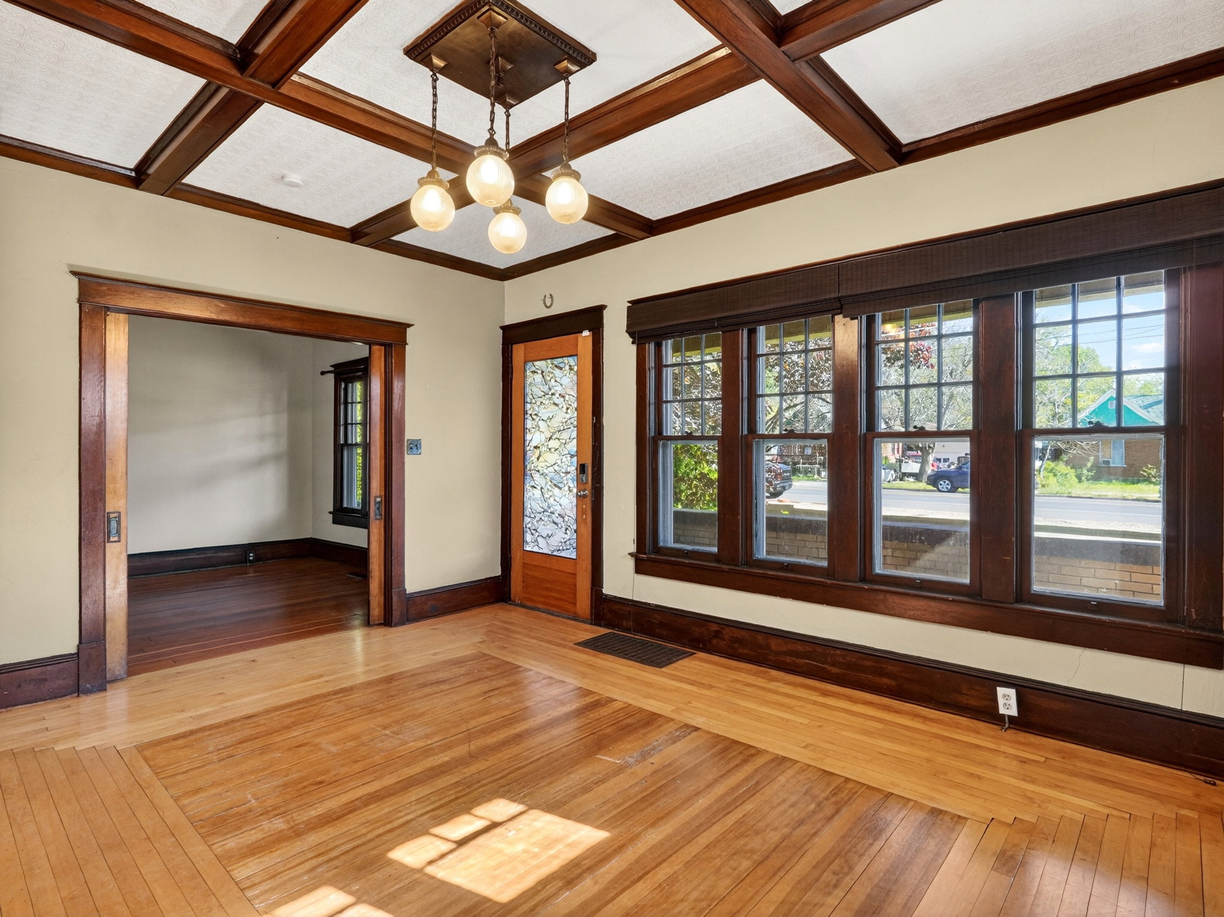 Hardwood flooring with a decorative inlay, coffered ceiling, and a multi-pane window wall with rich wood trim