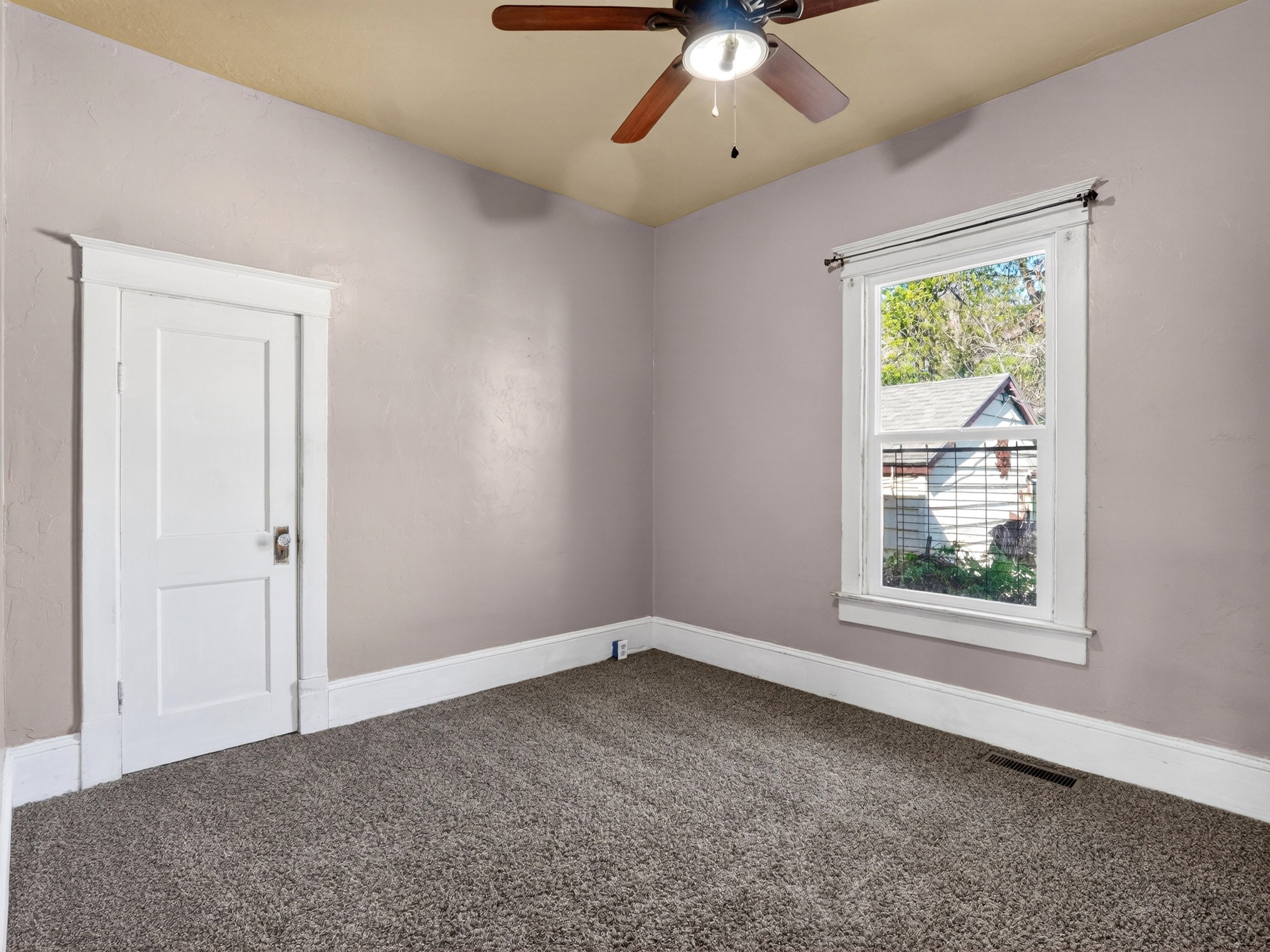 Carpeted room featuring a ceiling fan with light, a white paneled door with trim, and a window with white trim