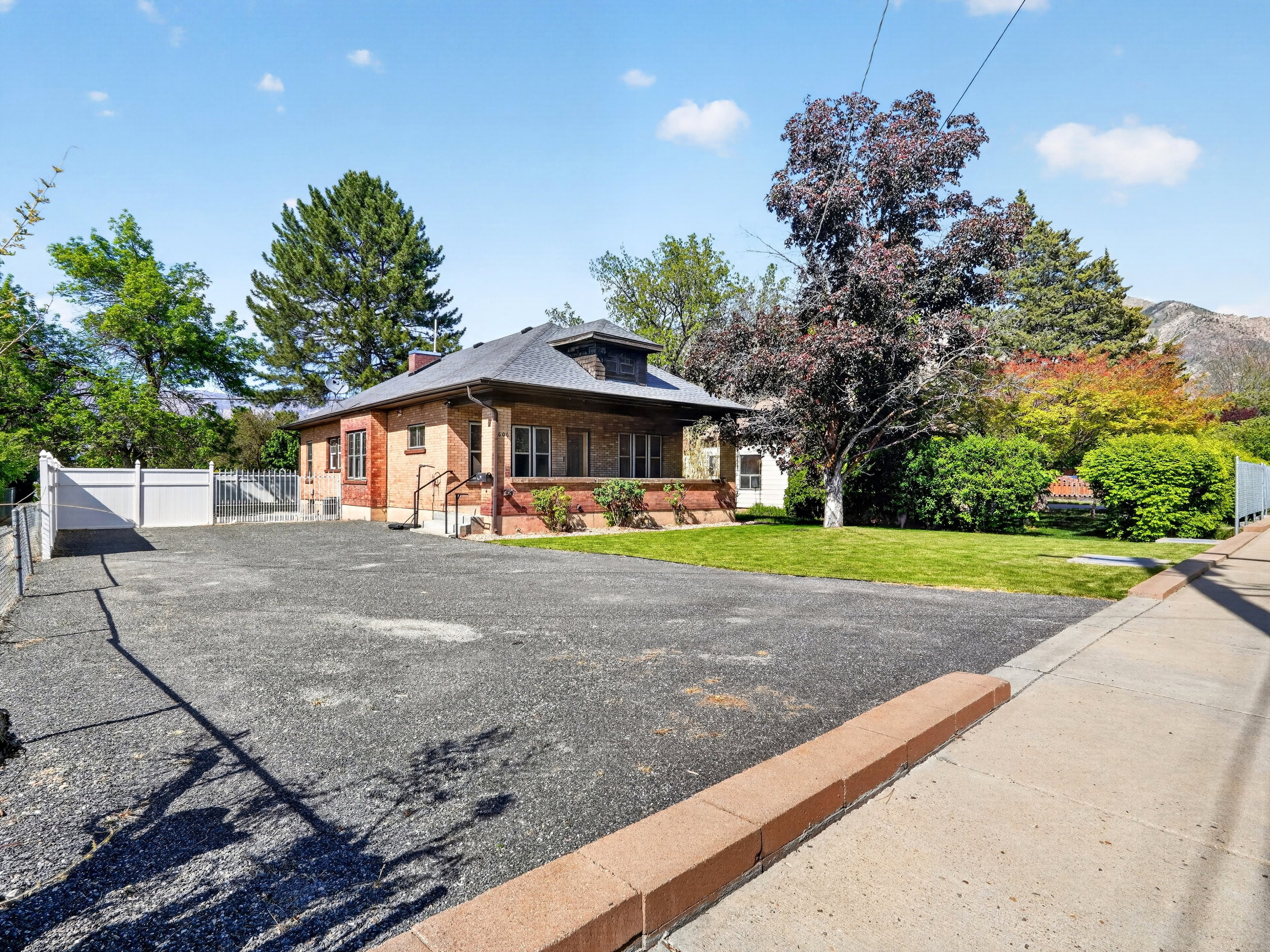 Brick exterior residence featuring a gabled roof, a gravel driveway, and an expansive lawn