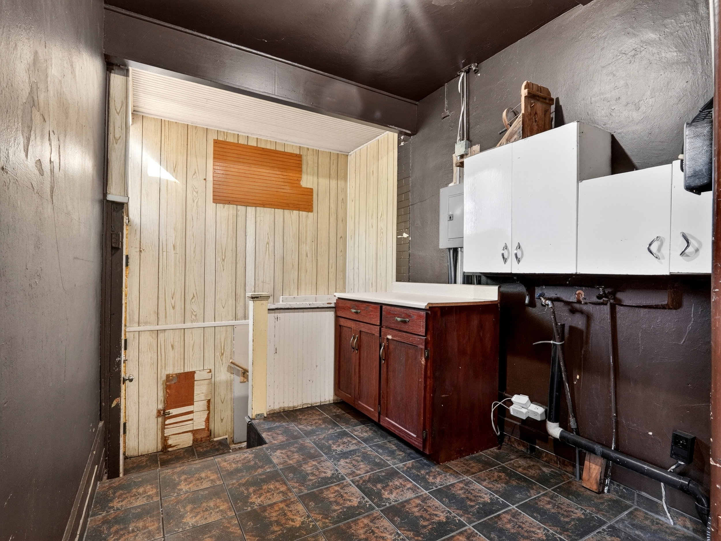 Utility area featuring a dark brown wall finish, white upper cabinetry with chrome hardware, and a wood-finish base cabinet with a light-colored countertop