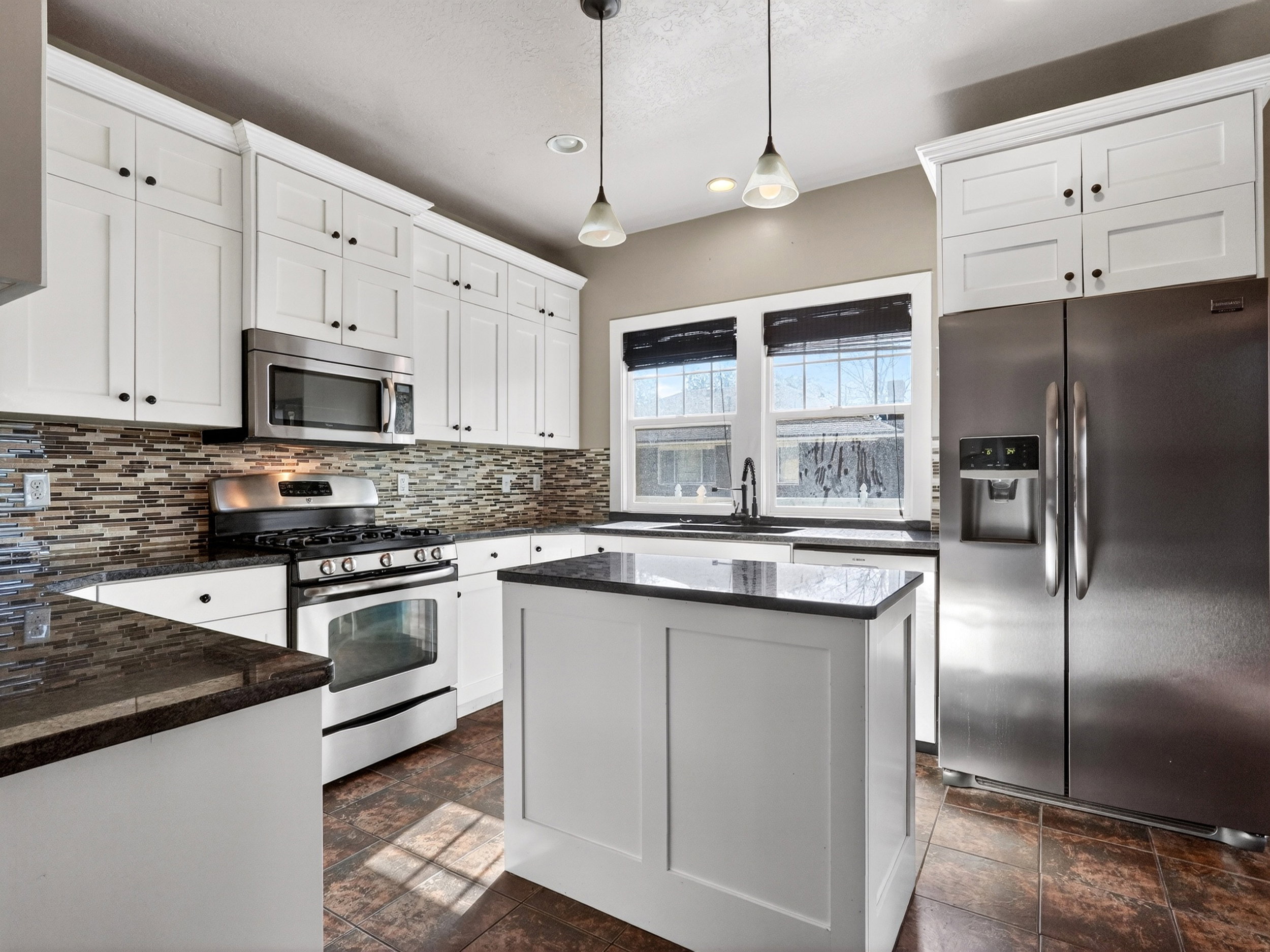Contemporary kitchen featuring white shaker cabinetry, stainless steel appliances, dark countertops, a mosaic tile backsplash, and a central island