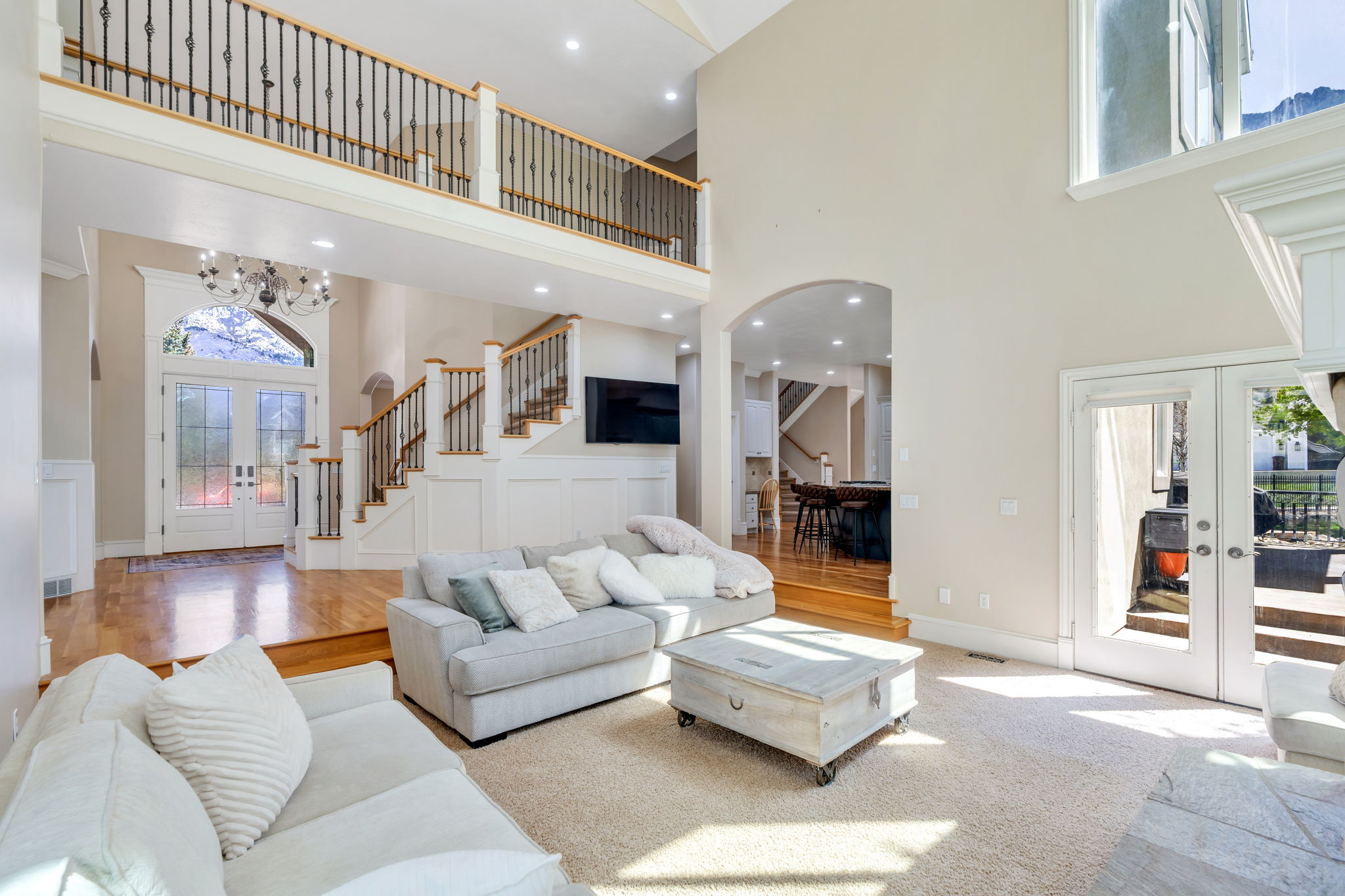 Vaulted great room with a second-story overlook, multiple large windows, and direct access to an outdoor patio through double French doors