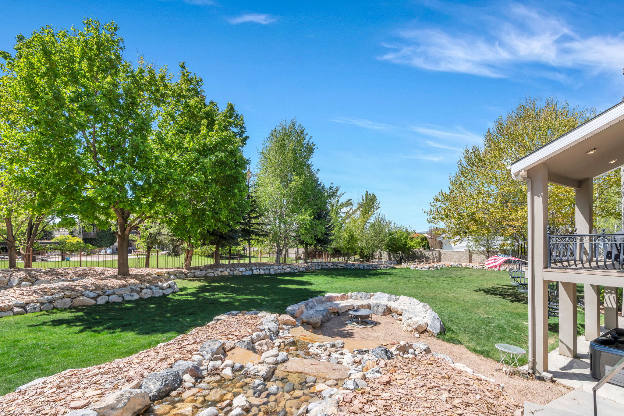 Expansive backyard featuring a large lawn area, mature trees, rock landscaping, and a built-in stone fire pit