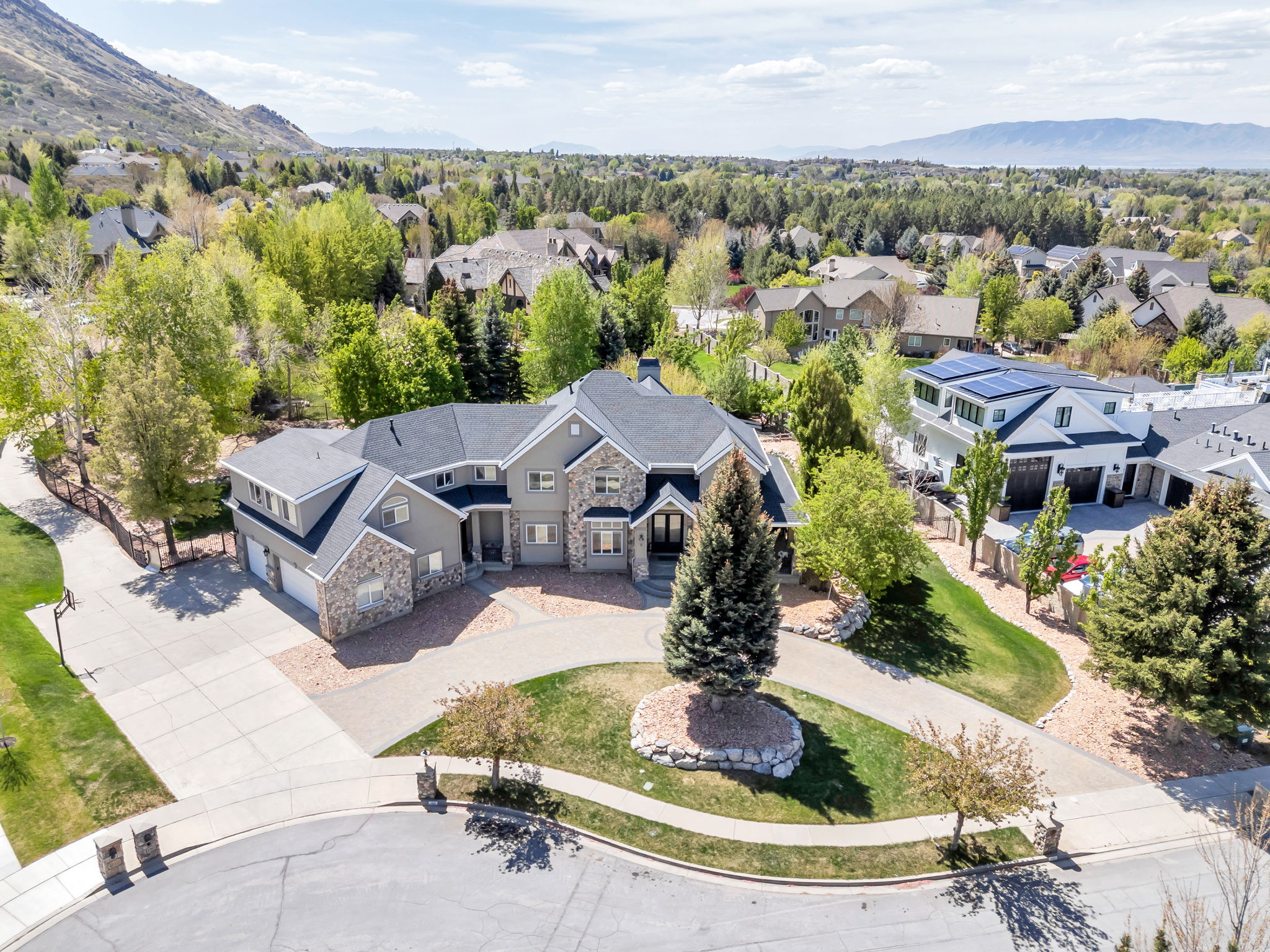 Spacious property featuring a stone and siding exterior, multiple garage bays, a circular driveway, and mature landscaping