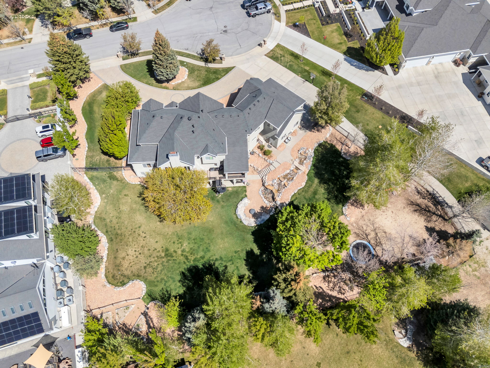 Expansive property featuring a multi-level residence with a dark shingle roof, a terraced stone hardscape, and a substantial green lawn