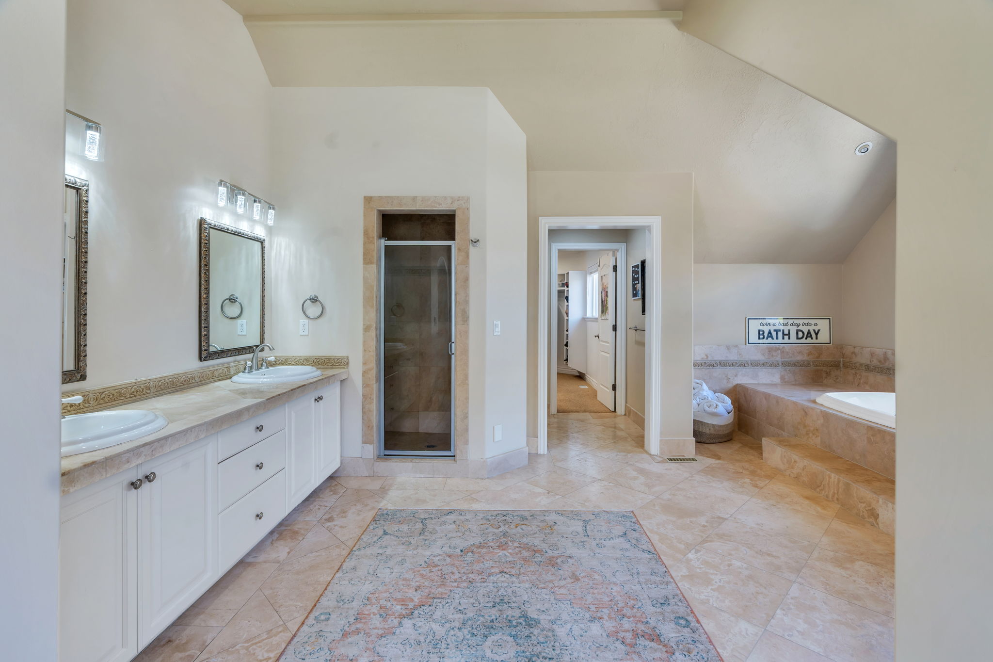 Spacious bathroom featuring twin vanity sinks, a tiled countertop, a glass-enclosed shower, a built-in soaking tub, and tile flooring