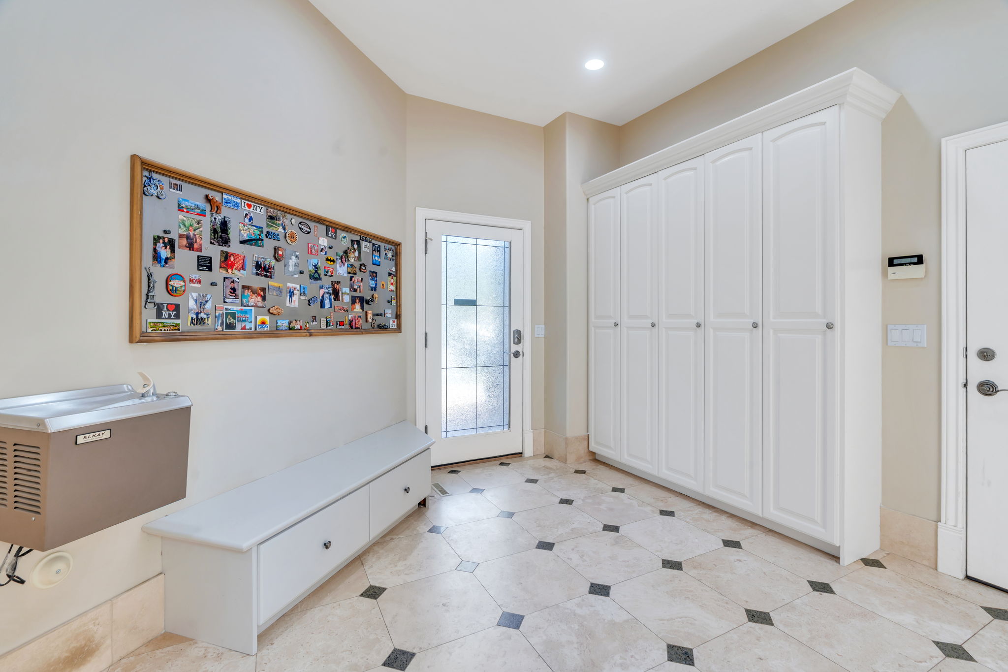 Entryway featuring extensive built-in cabinetry, decorative glass-paneled door, recessed lighting, and tile flooring with accent inserts