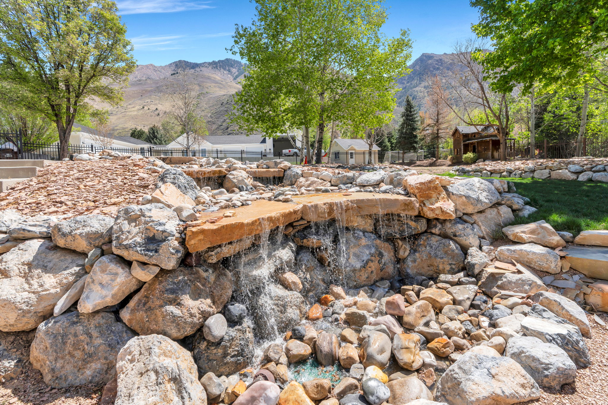 Rock water feature with multiple cascades, surrounded by natural stone landscaping and mature trees