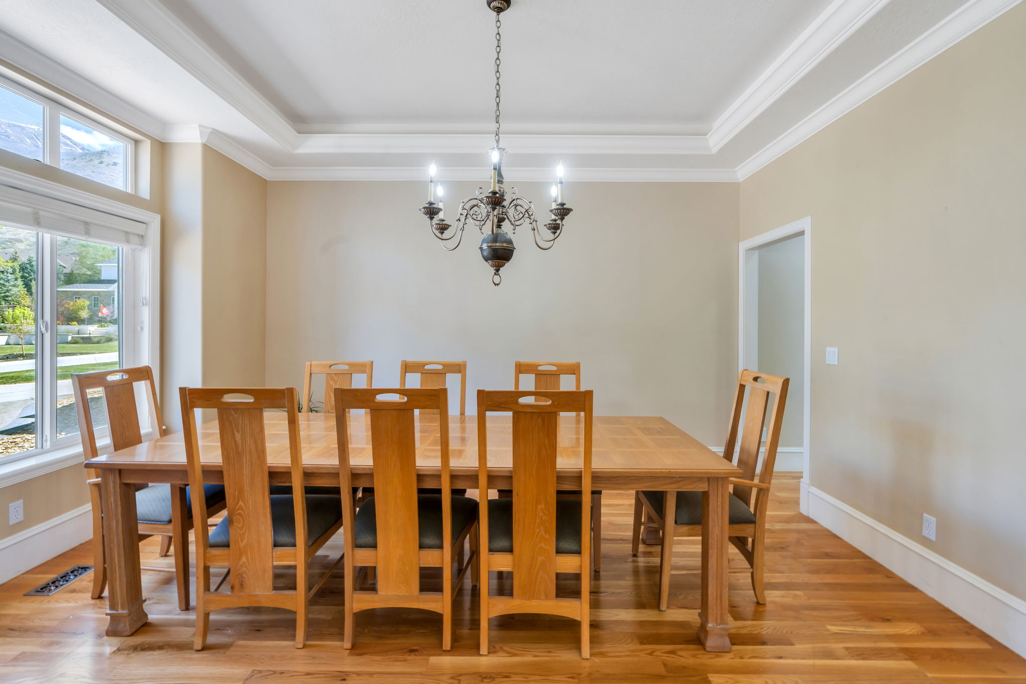 Dining area featuring wood-finish flooring, a multi-pane window, a chandelier, and a tray ceiling with crown molding