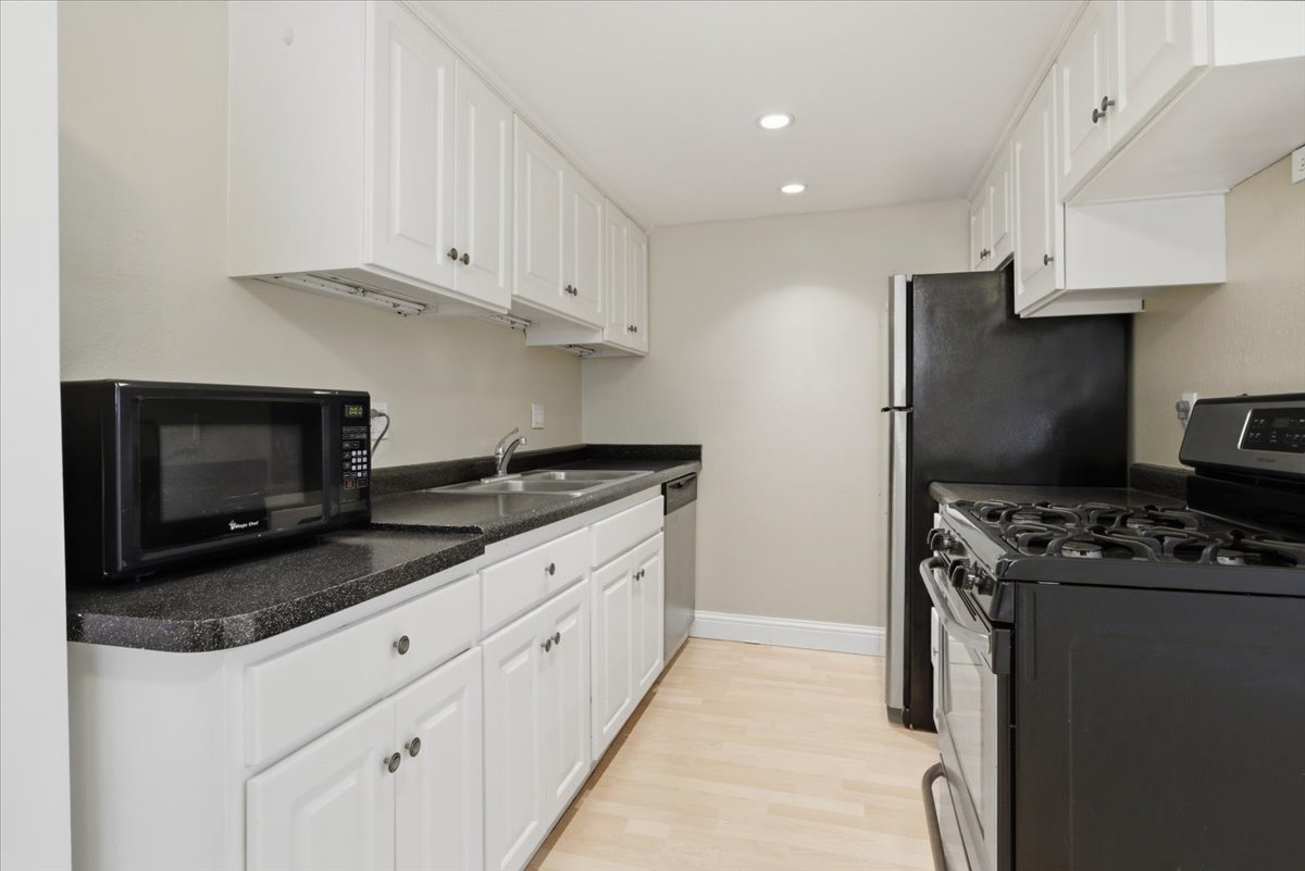 Galley kitchen featuring white cabinetry, dark countertops, a double basin sink, light wood-finish flooring, and recessed lighting