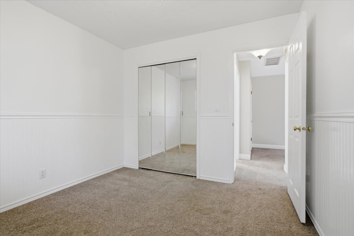 Bedroom featuring mirrored sliding closet doors, wainscoting, neutral carpeting, and white trim