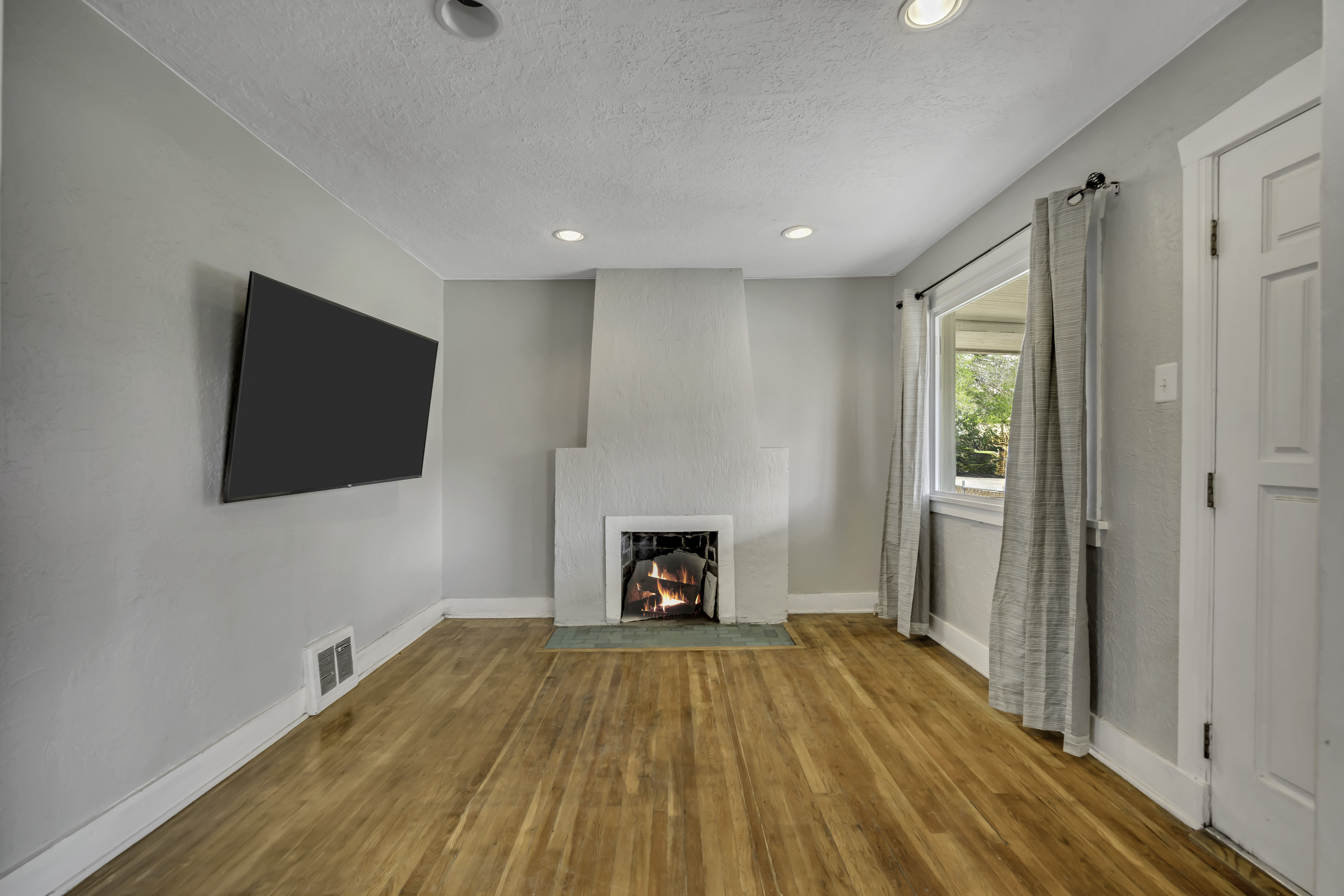 Living area featuring wood-finish flooring, a fireplace with a light-colored surround, recessed lighting, and a wall-mounted television