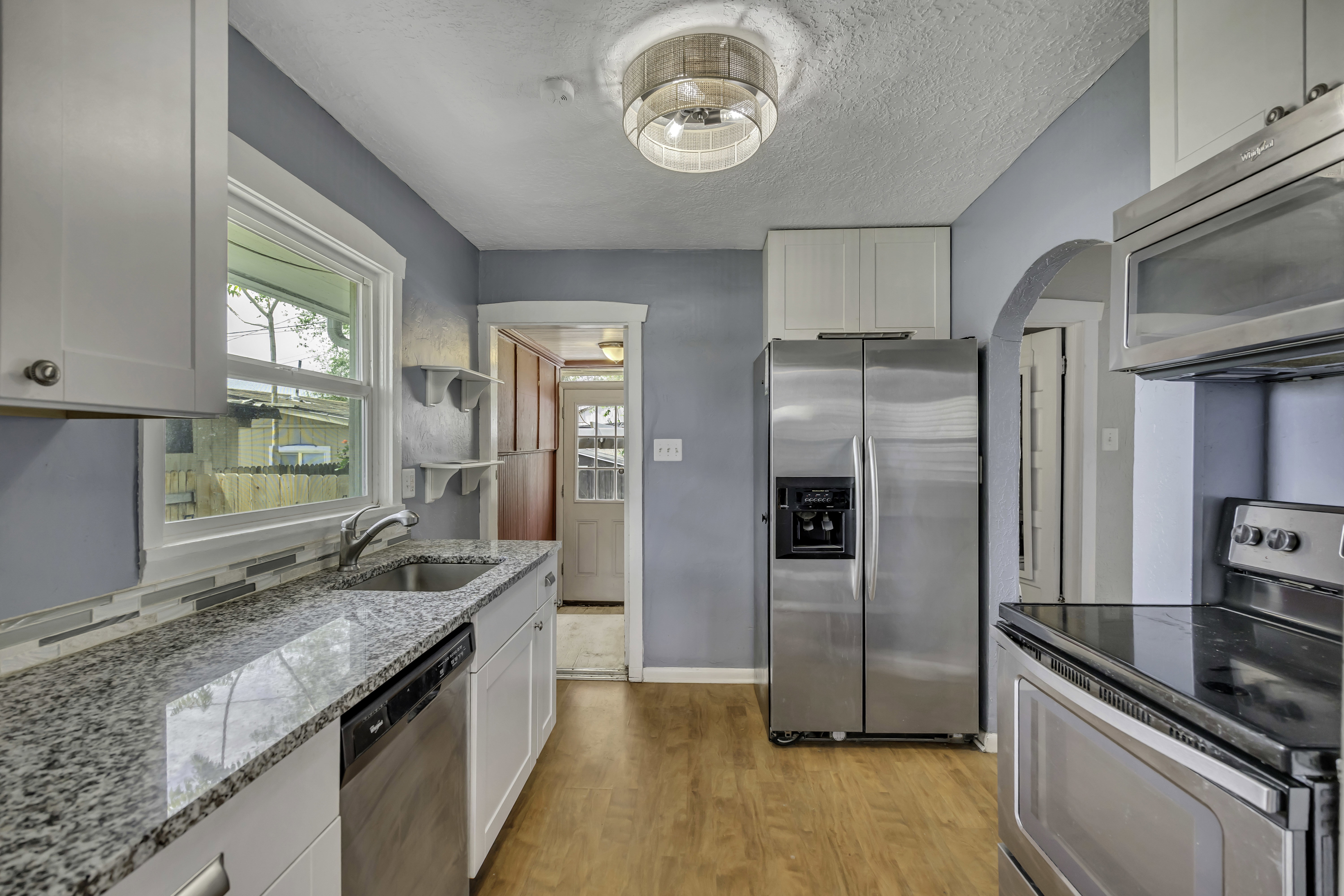 Kitchen featuring light wood-finish flooring, white cabinetry, speckled countertops, a double basin sink with a gooseneck faucet, and stainless steel appliances including a refrigerator, dishwasher, and stove