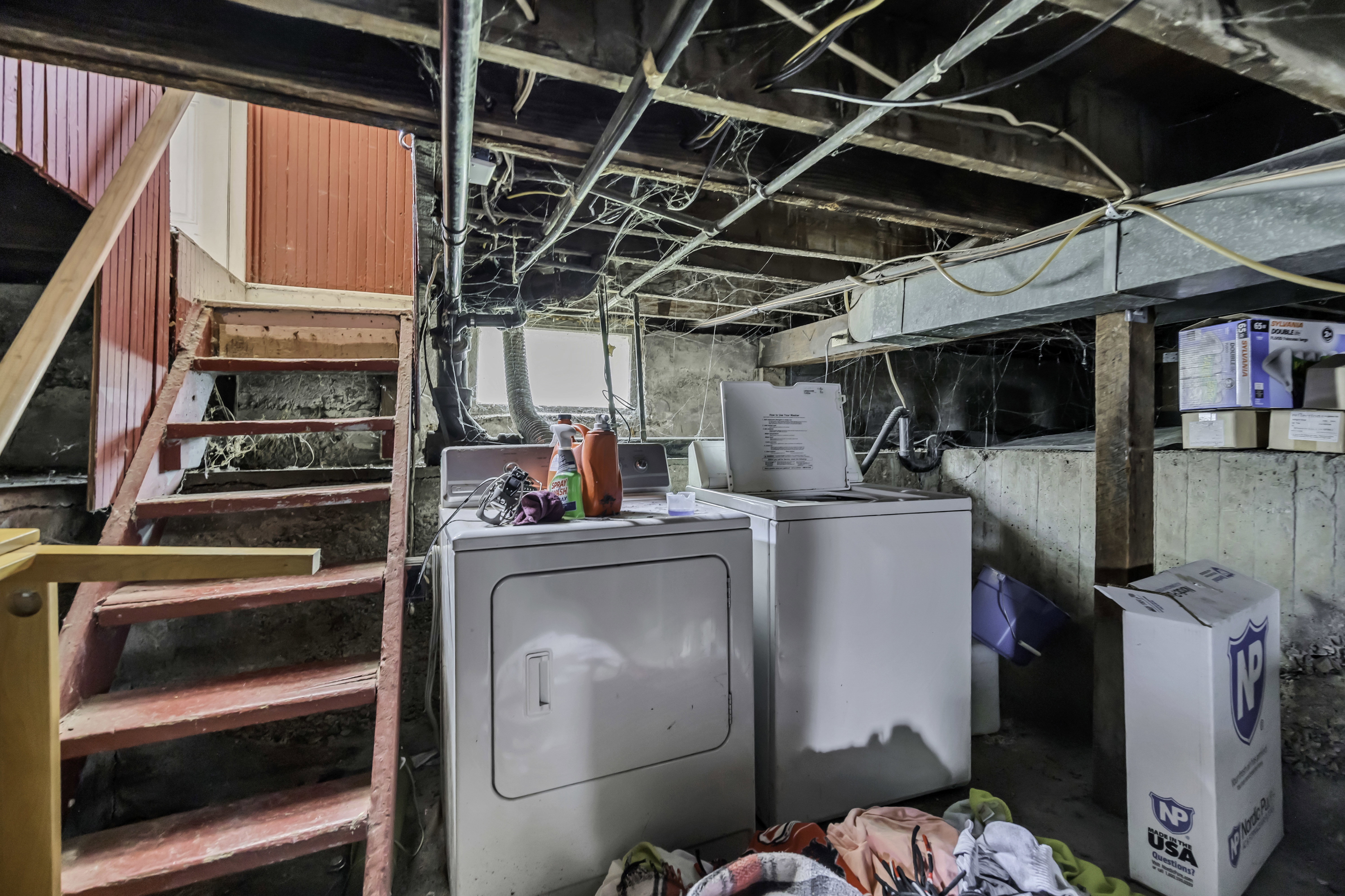 Basement utility area featuring exposed joists, concrete walls, a wooden staircase with red painted risers, and an installed washer and dryer unit