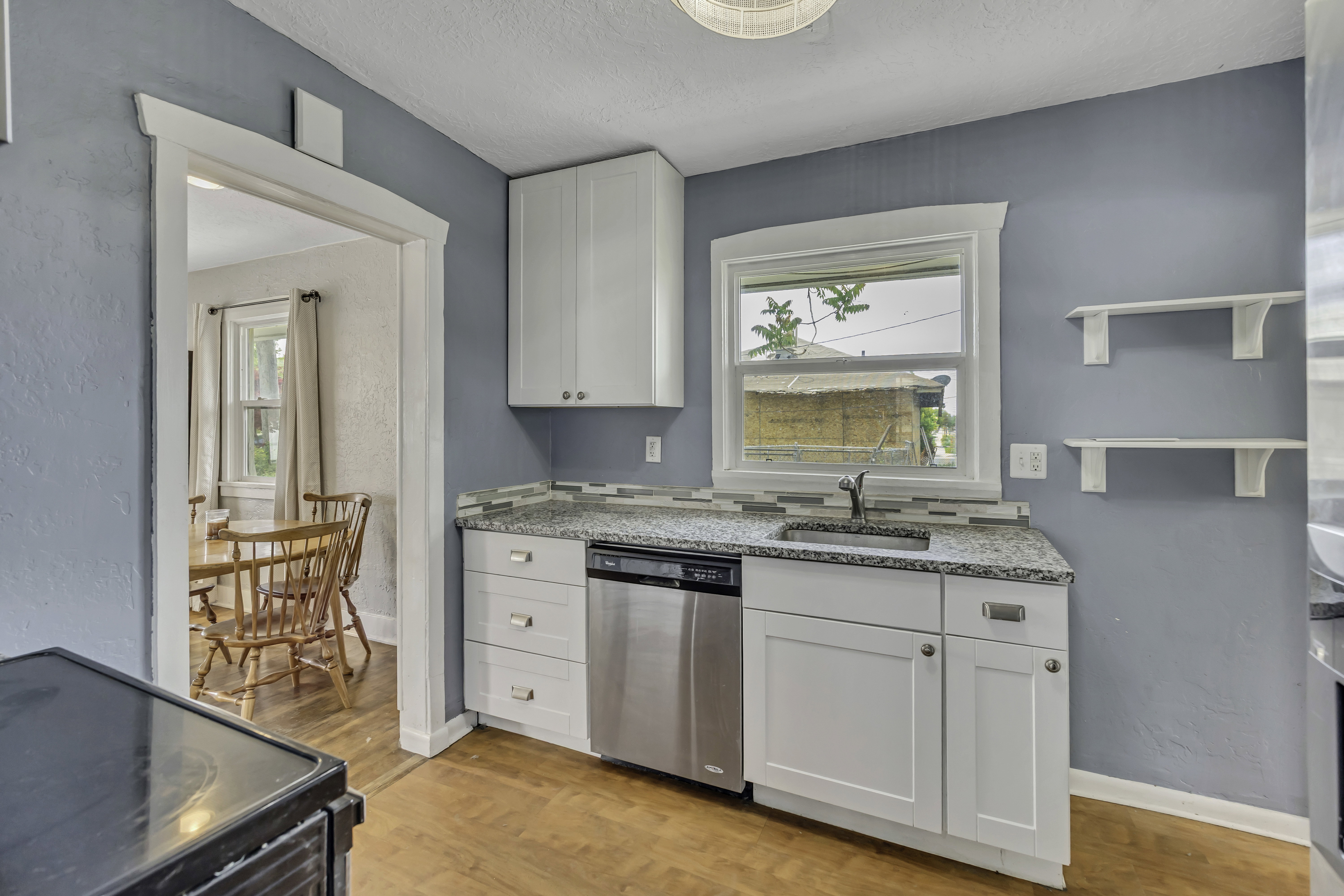 Kitchen featuring white cabinetry, a stainless steel dishwasher, a countertop with an integrated sink, a tile backsplash, and wood-finish flooring
