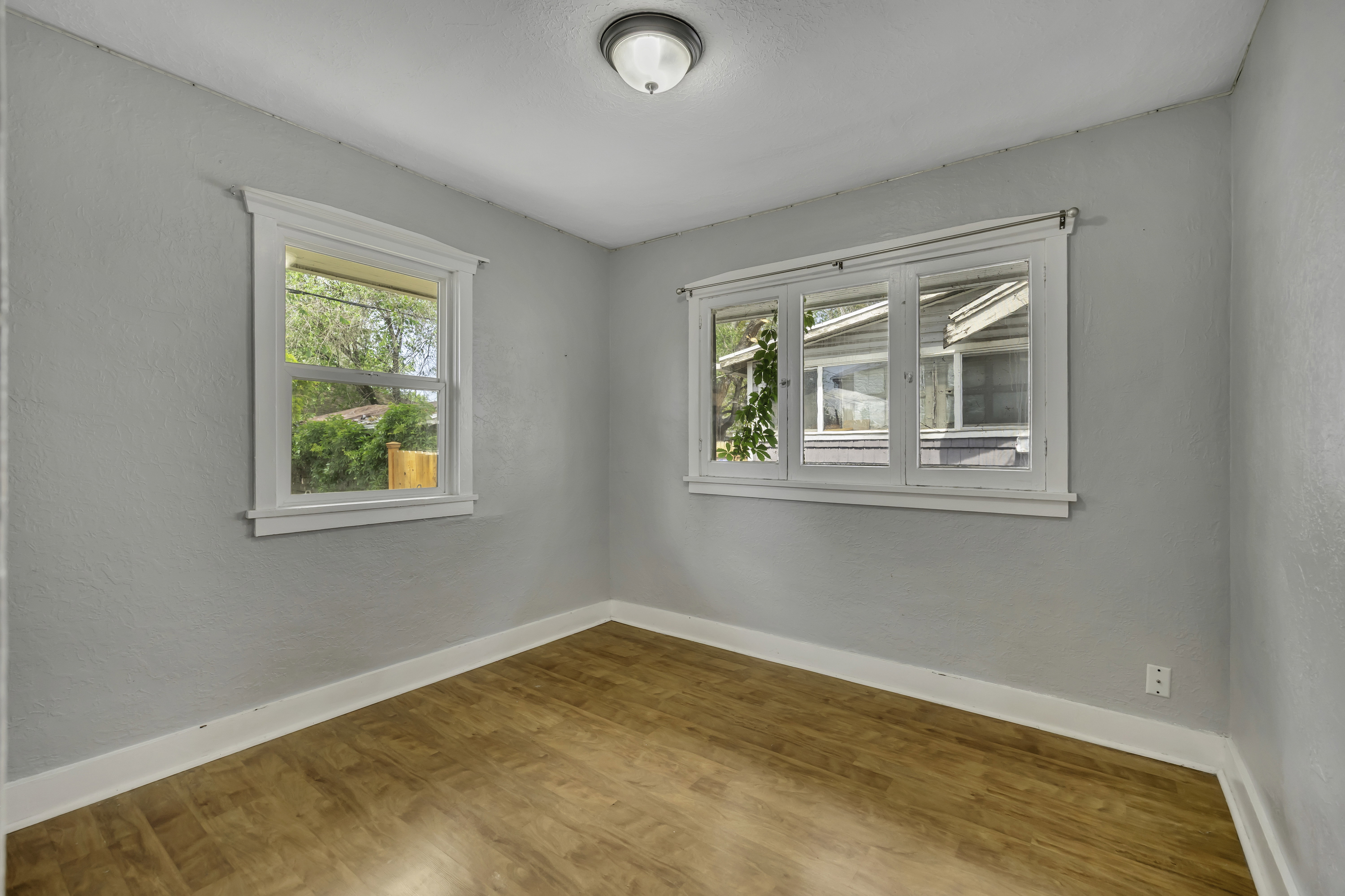 Light-filled room featuring wood-finish flooring, white baseboards, and two windows with white trim
