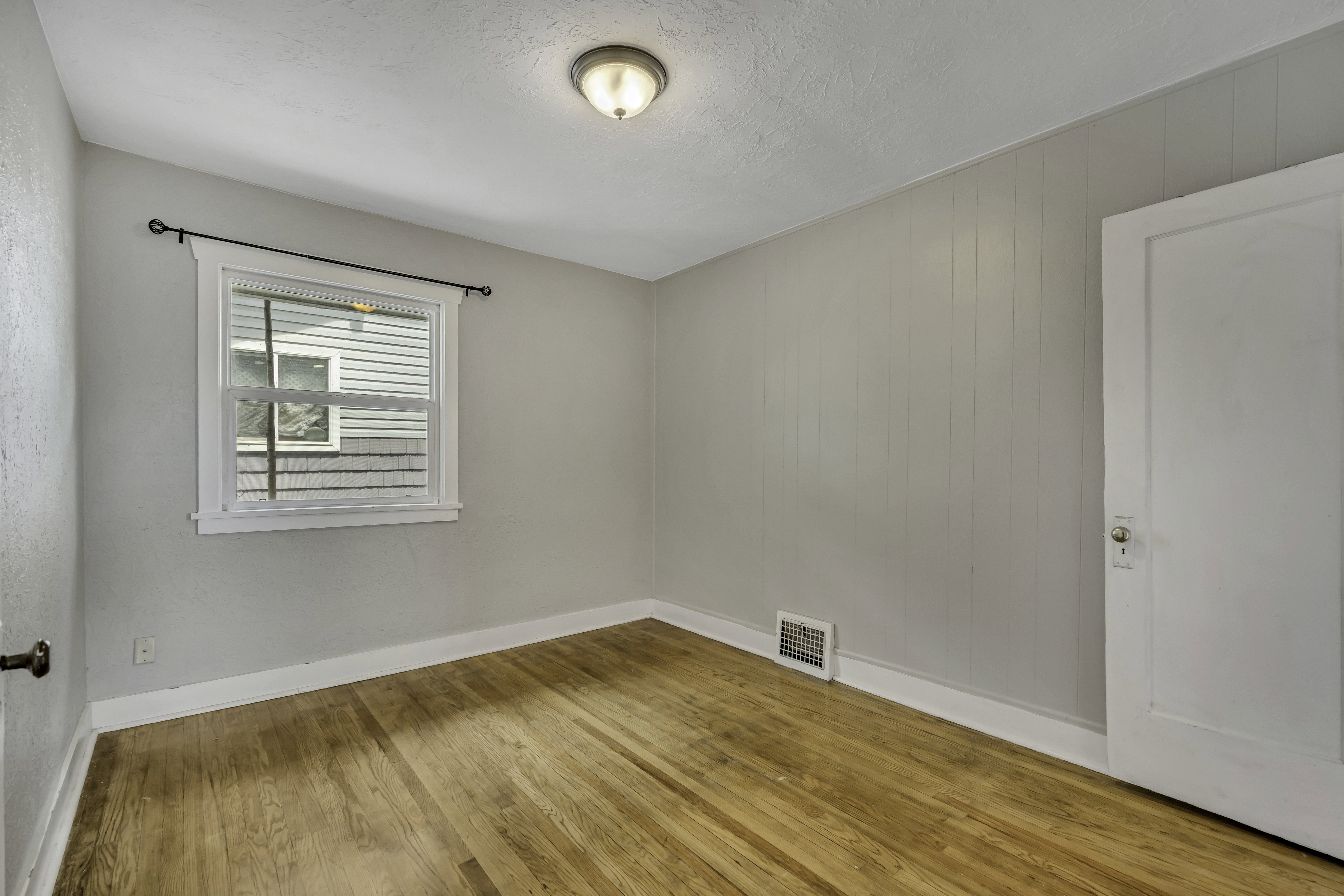 Bedroom featuring wood-finish flooring, white trim, a double-hung window, wall paneling, and a flush-mount ceiling light