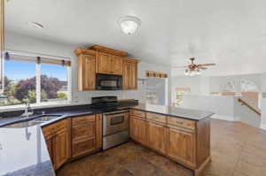 Kitchen featuring wood cabinetry, stainless steel appliances, dark stone countertops, and a double basin sink