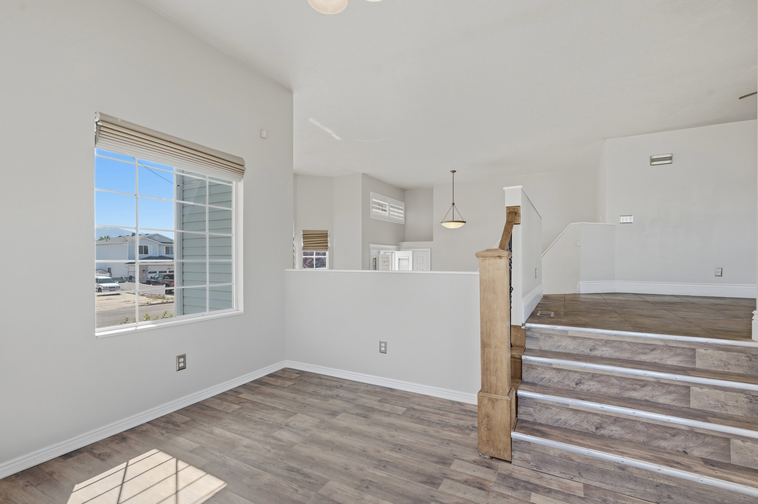 Spacious room featuring wood-finish flooring, a large multi-pane window with a roller shade, and a half-wall partition