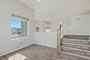 Spacious room featuring wood-finish flooring, a large multi-pane window with a roller shade, and a half-wall partition