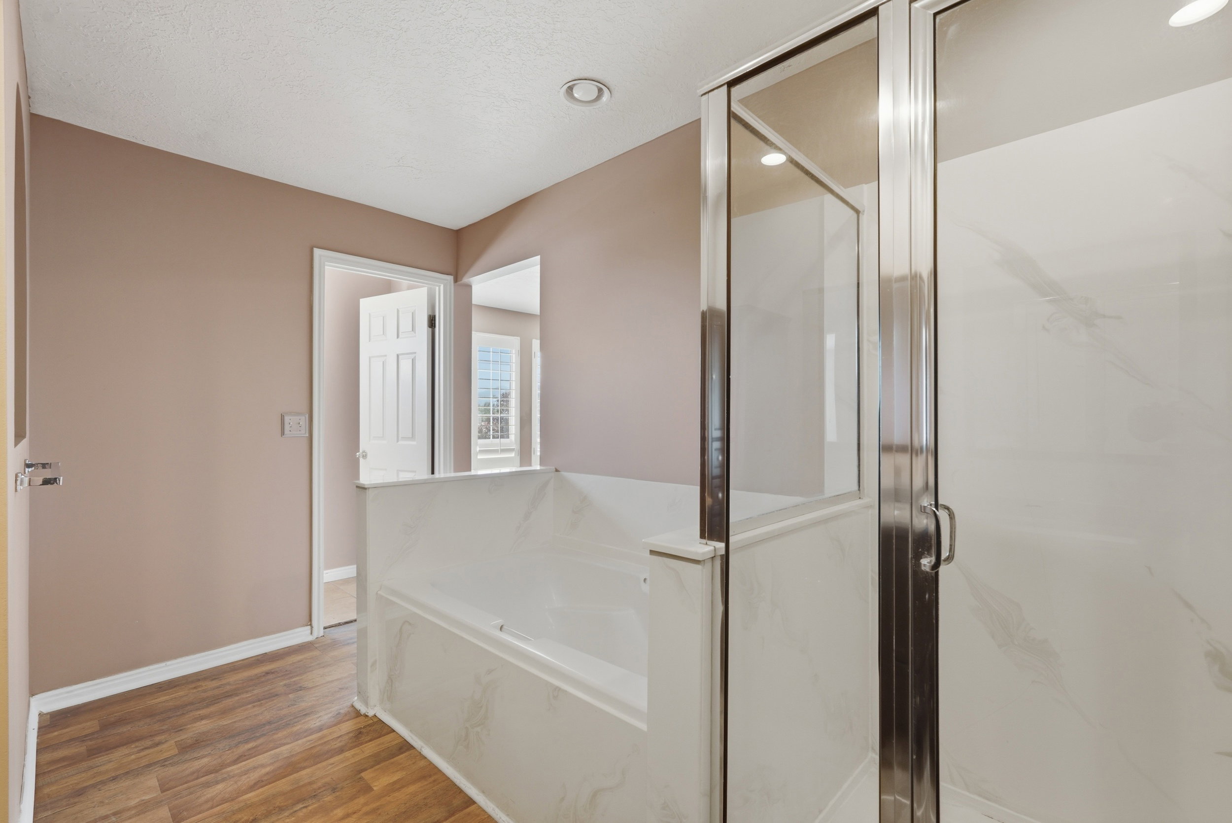 Bathroom featuring a built-in tub with a white surround and an adjacent glass-enclosed shower with white paneling