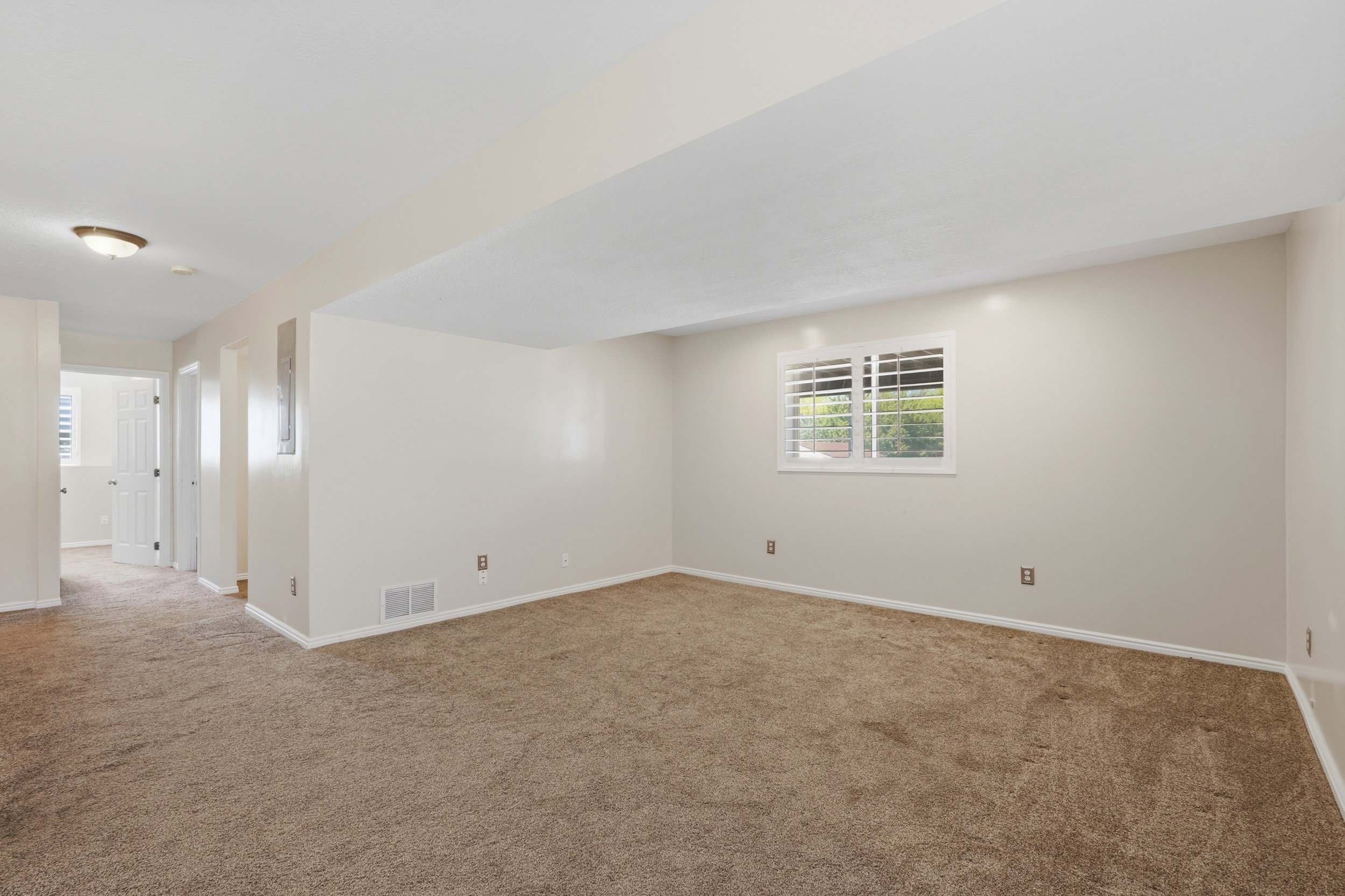 Carpeted interior space featuring neutral wall tones, white baseboards, and a window with white plantation shutters