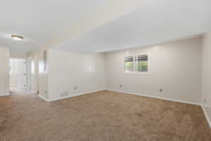 Carpeted interior space featuring neutral wall tones, white baseboards, and a window with white plantation shutters