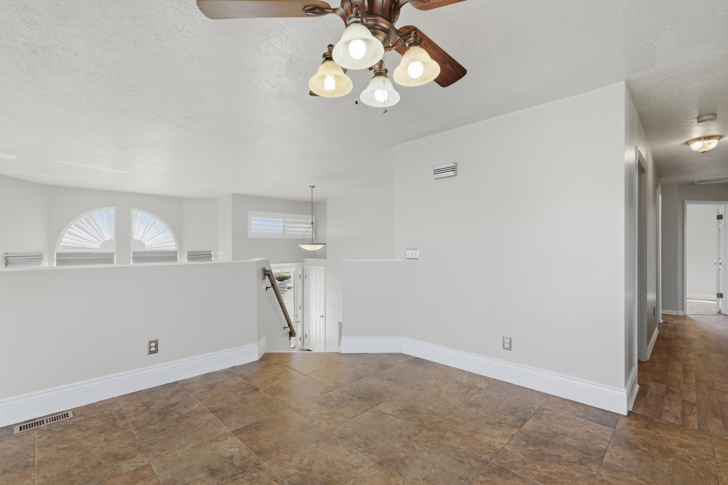 Spacious upper-level landing featuring durable tile-look flooring, a ceiling fan with integrated lighting, and a partial wall overlooking the lower level