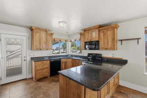 Kitchen featuring wood-finish cabinetry with crown molding, dark stone-finish countertops, black appliances, and tile flooring