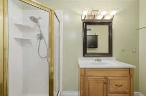 Bathroom featuring a corner shower with a gold-toned frame, a wood-finish vanity with a white countertop, a rectangular sink, and a framed mirror